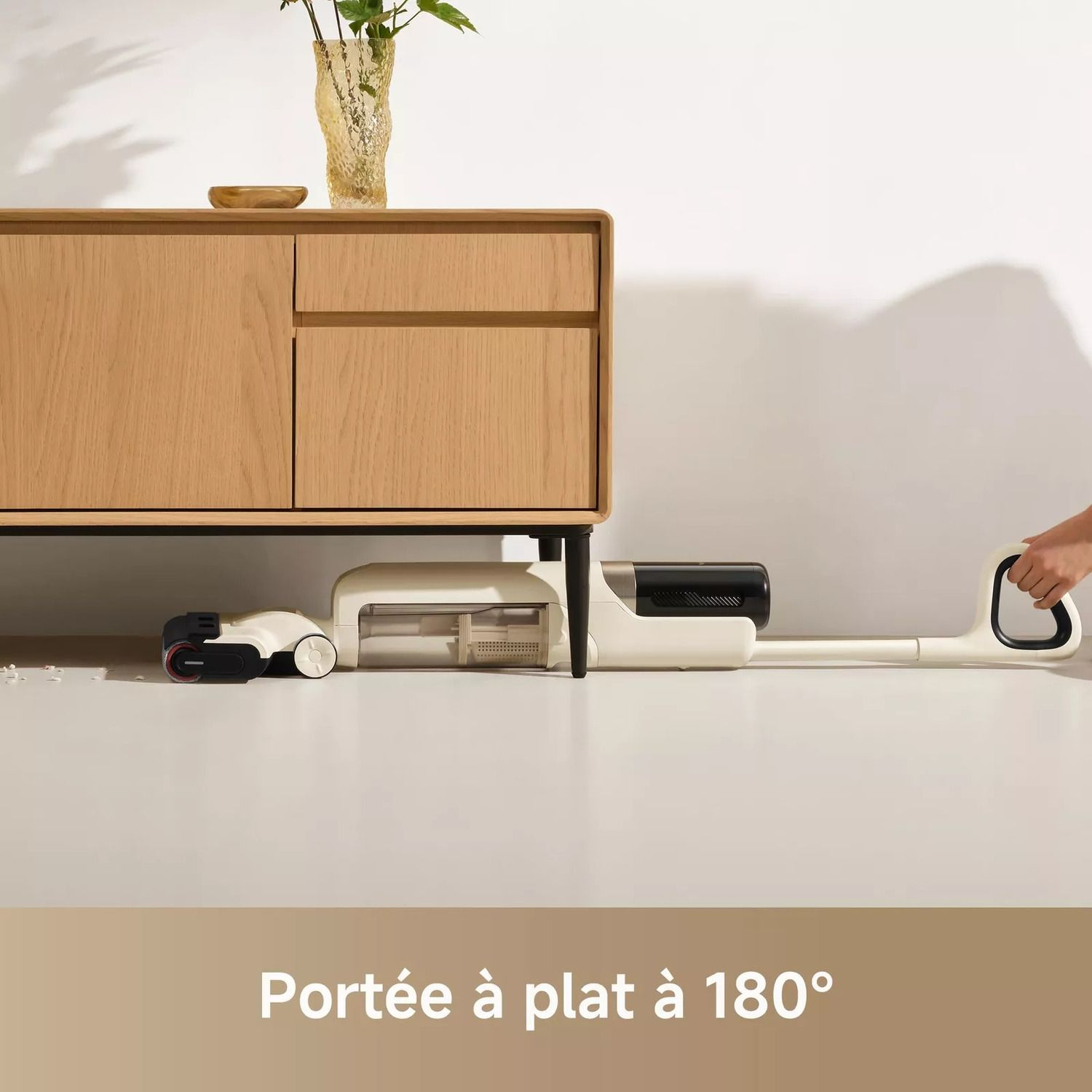 Aspirateur blanc et noir sous un meuble en bois sur un sol blanc.