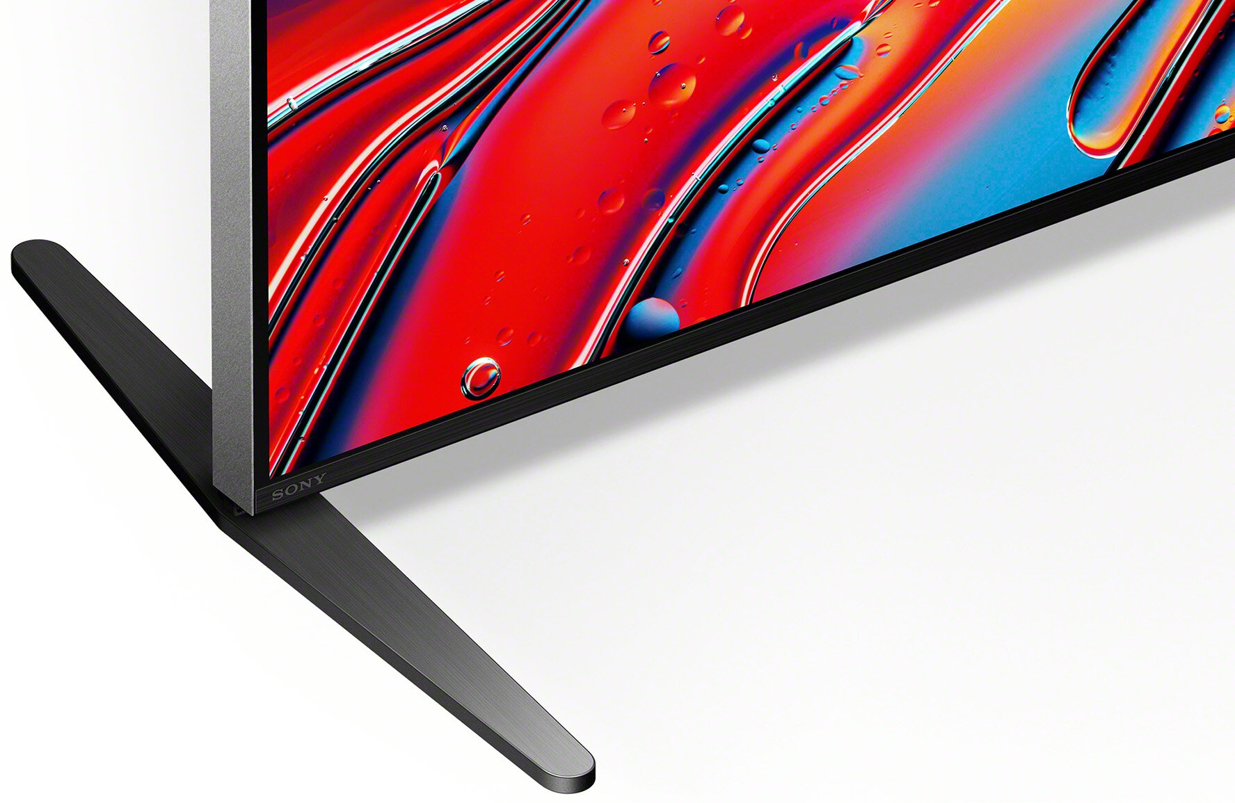 Zbliżenie rogu telewizora. Wyświetlacz pokazuje kolorową sztukę abstrakcyjną, czarna podstawa.