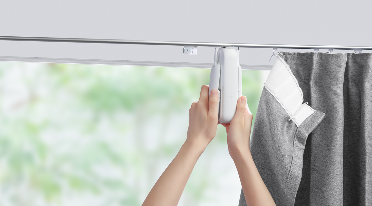 Hände installieren einen weißen Vorhangmotor an einer Gardinenstange. Verschwommene Fensteransicht.
