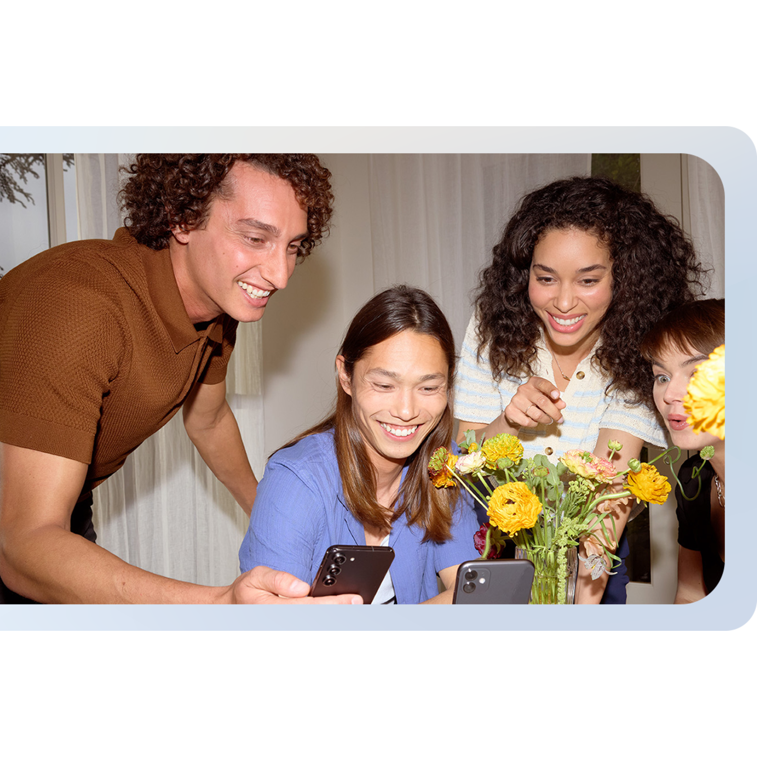 Group of friends smiles looking at phones, flowers on table.