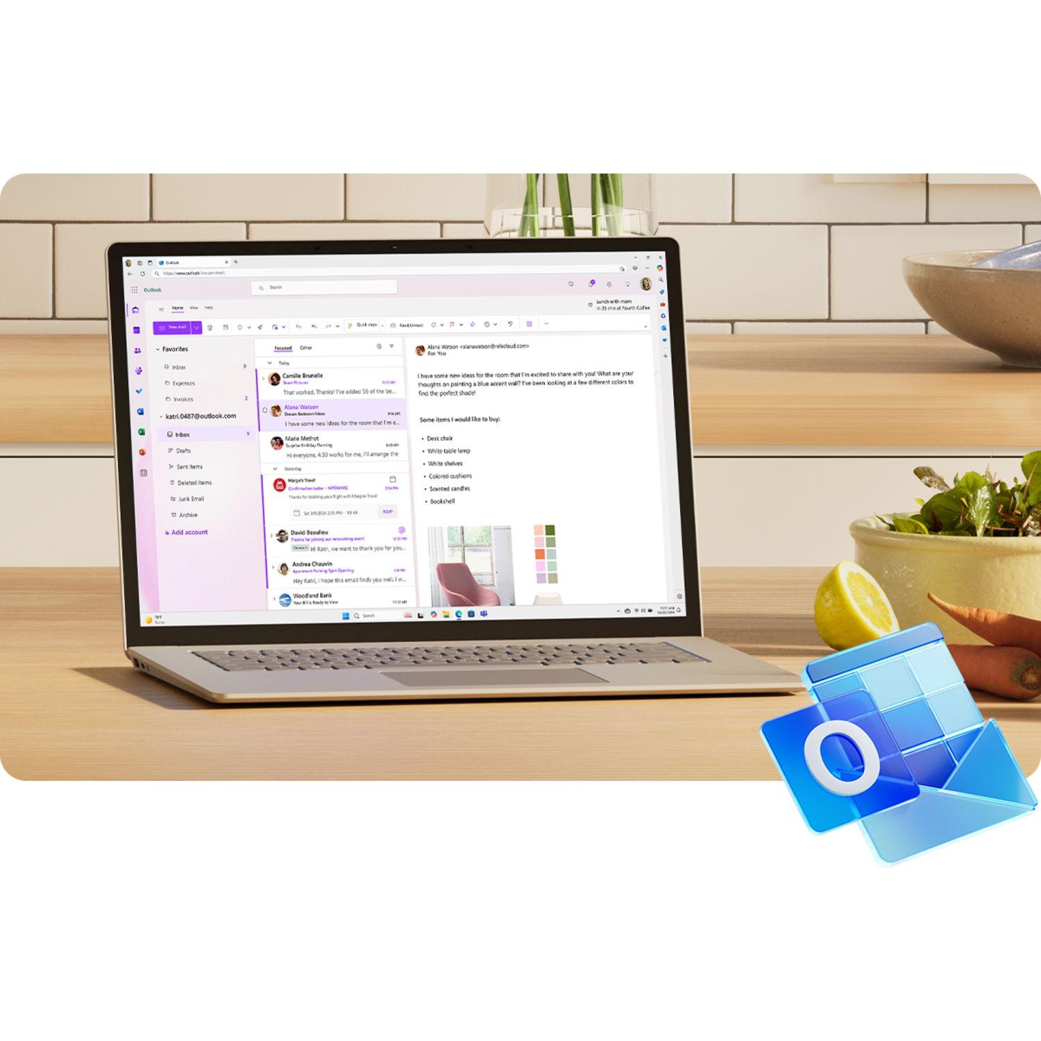 Laptop displaying an Outlook email inbox. A bowl, a lemon, and other items are on the table.