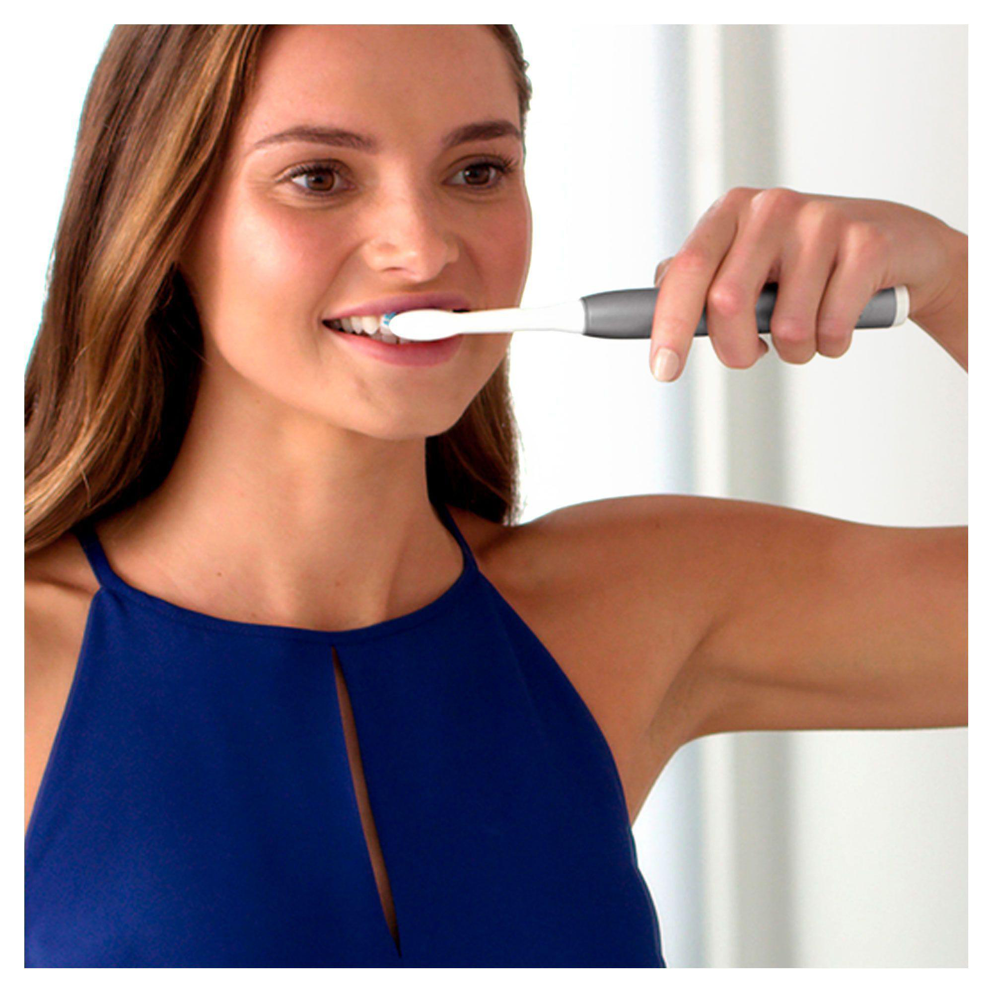 Frau putzt Zähne mit elektrischer Zahnbürste, Nahaufnahme, blaues Kleid.