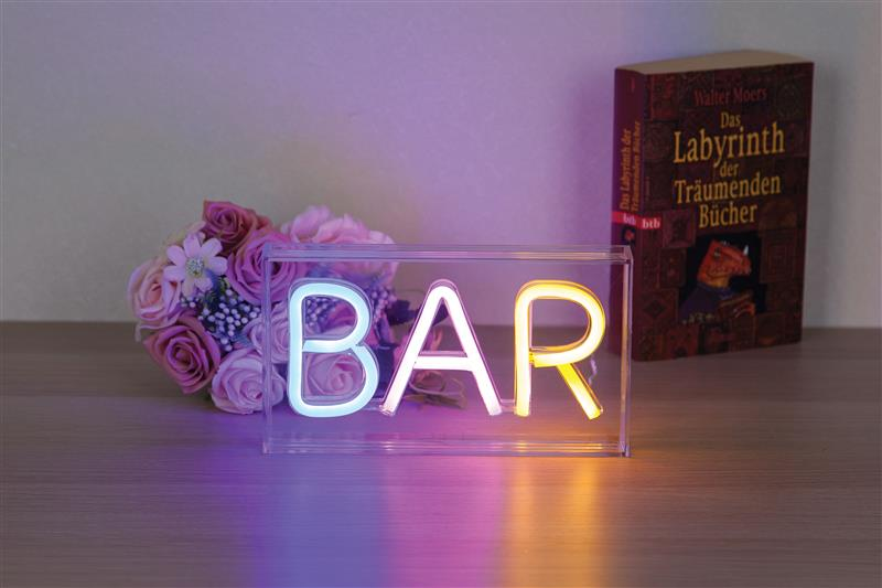 Neonowy znak "BAR" w szklanym pudełku obok kwiatów i książki.