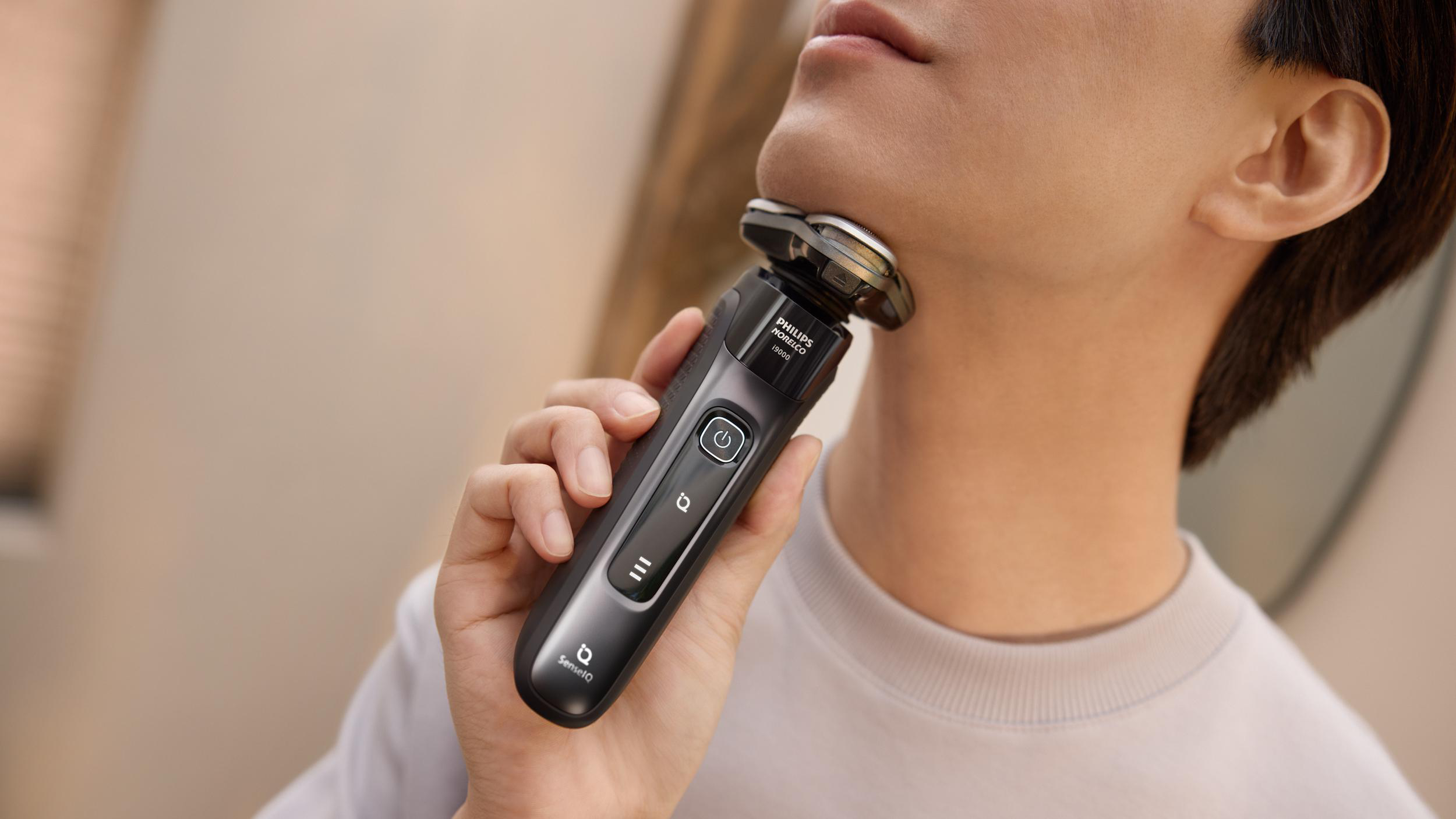 Ein Mann rasiert sich den Hals mit einem elektrischen Rasierer. Der Rasierer ist schwarz und grau.