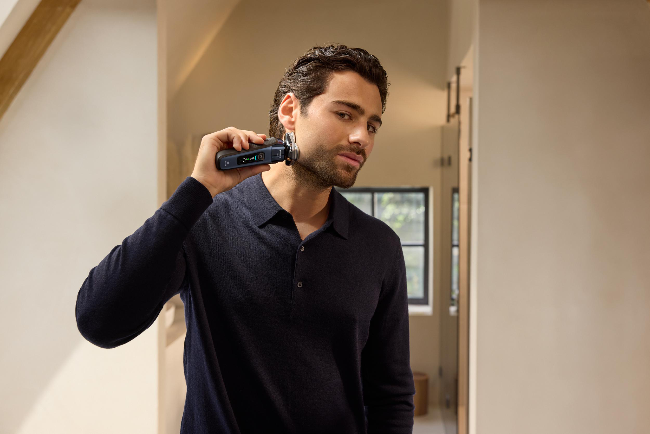 Ein Mann rasiert seinen Bart mit einem schwarzen Elektrorasierer in einem gut beleuchteten Raum.