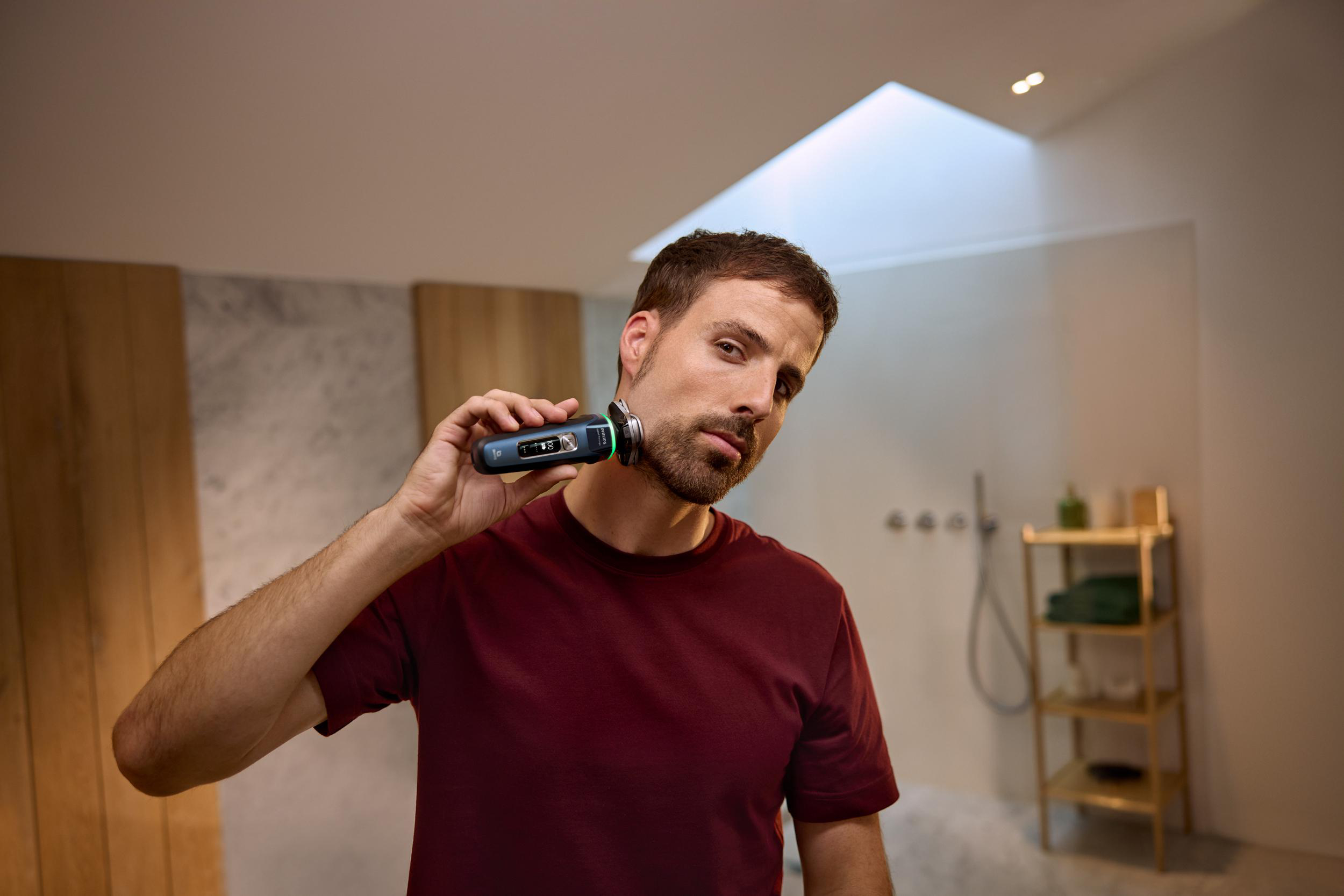 Mann rasiert Bart mit schwarzem und silbernem Elektrorasierer im Bad.