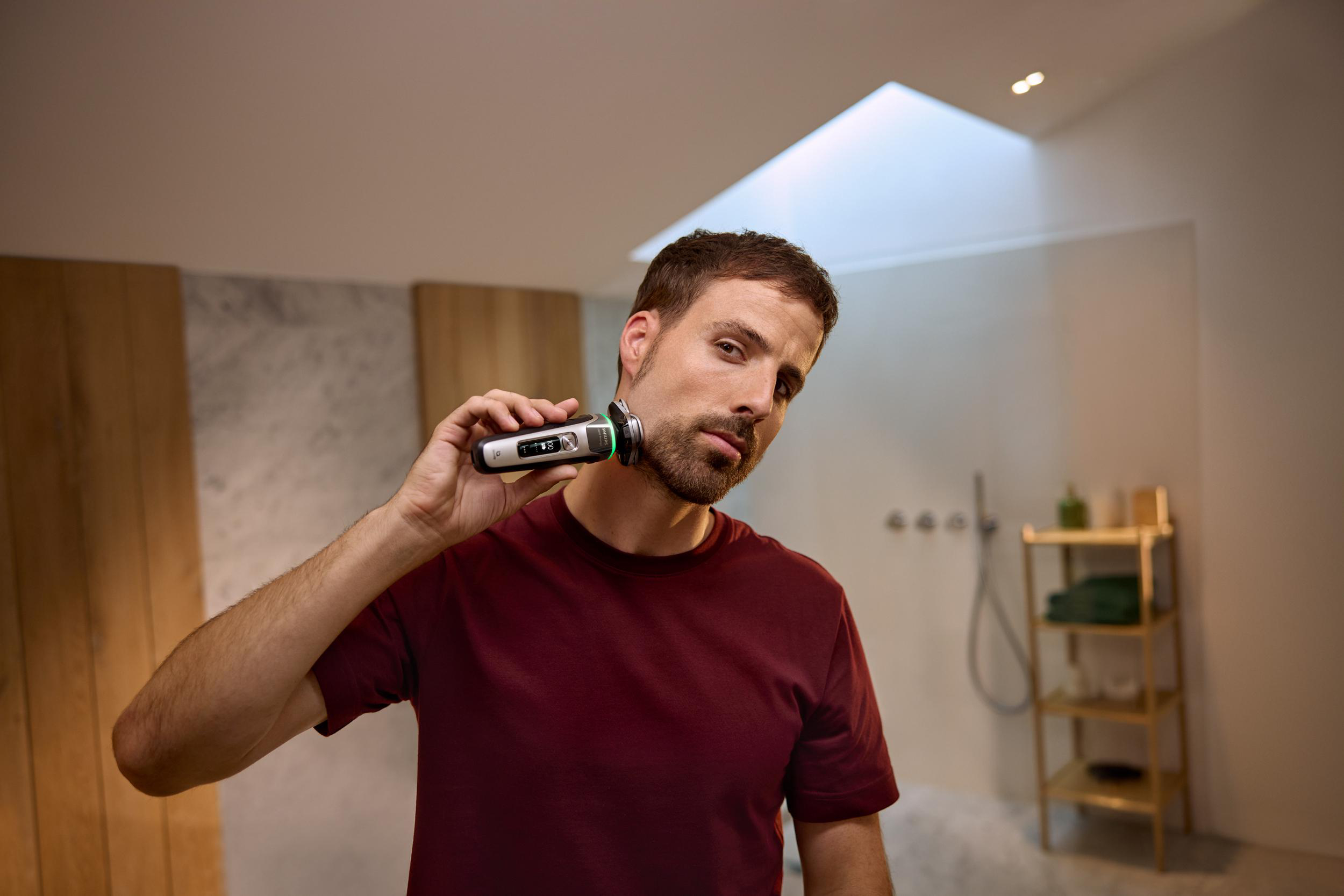 Ein Mann rasiert sich mit einem Elektrorasierer in einem gut beleuchteten Badezimmer.