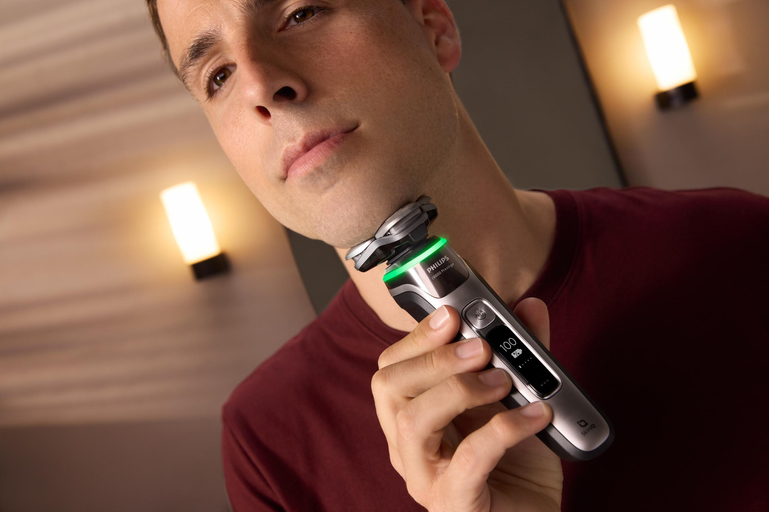 Mann rasiert sich mit einem Philips Elektrorasierer, mit zwei Wandleuchten hinter ihm.