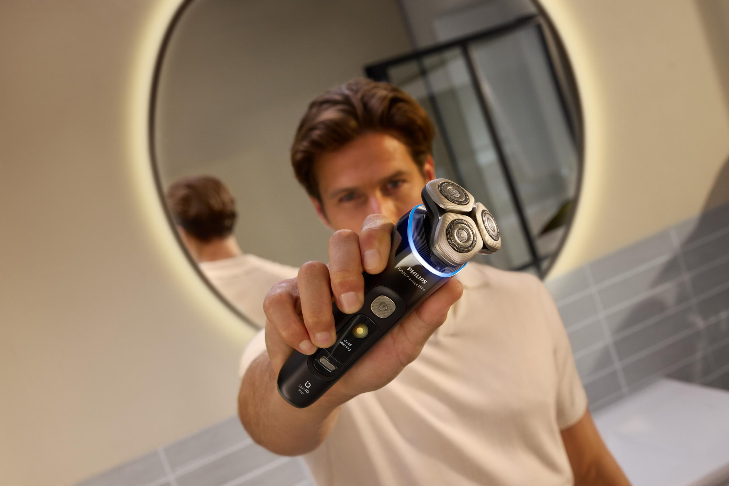 Mann hält einen schwarz-silbernen Elektrorasierer vor einem Spiegel.