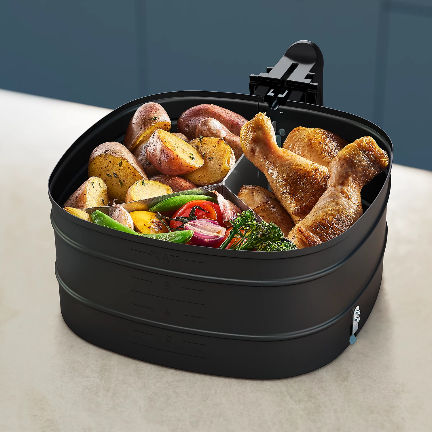 Schwarzer Airfryer-Korb mit gebratenem Gemüse und Hähnchenschenkeln.