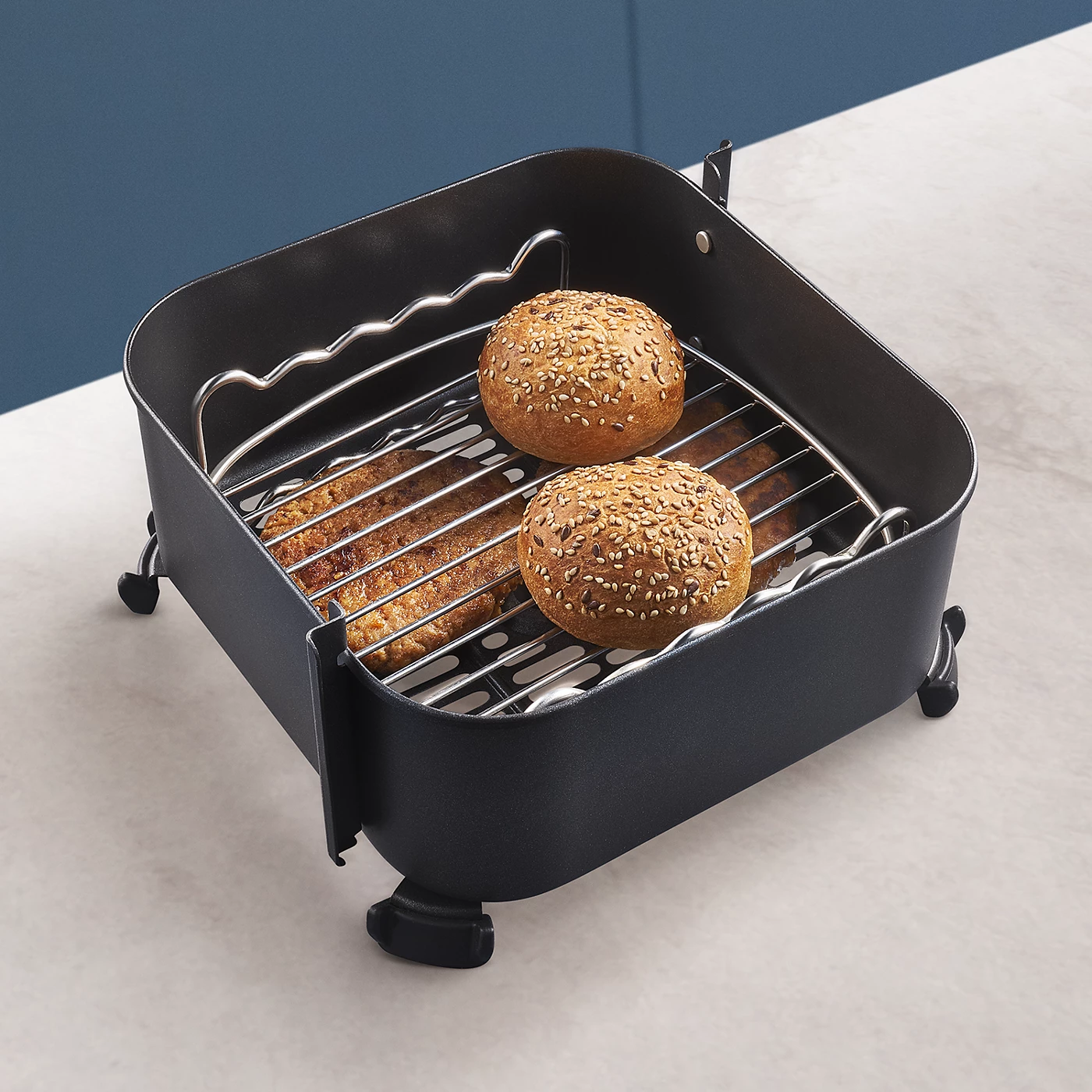 Schwarzes Airfryer-Zubehör mit Würstchen und Brötchen darin.