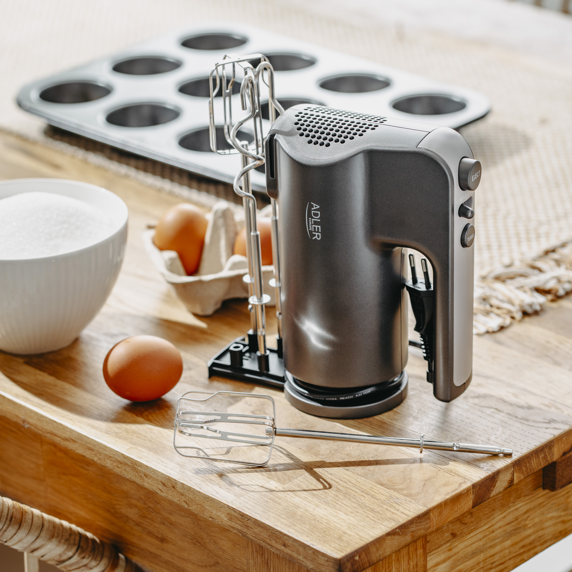 Kézi mixer, tojások, muffin sütőforma, cukortartó a faasztalon. Konyhai beállítás.