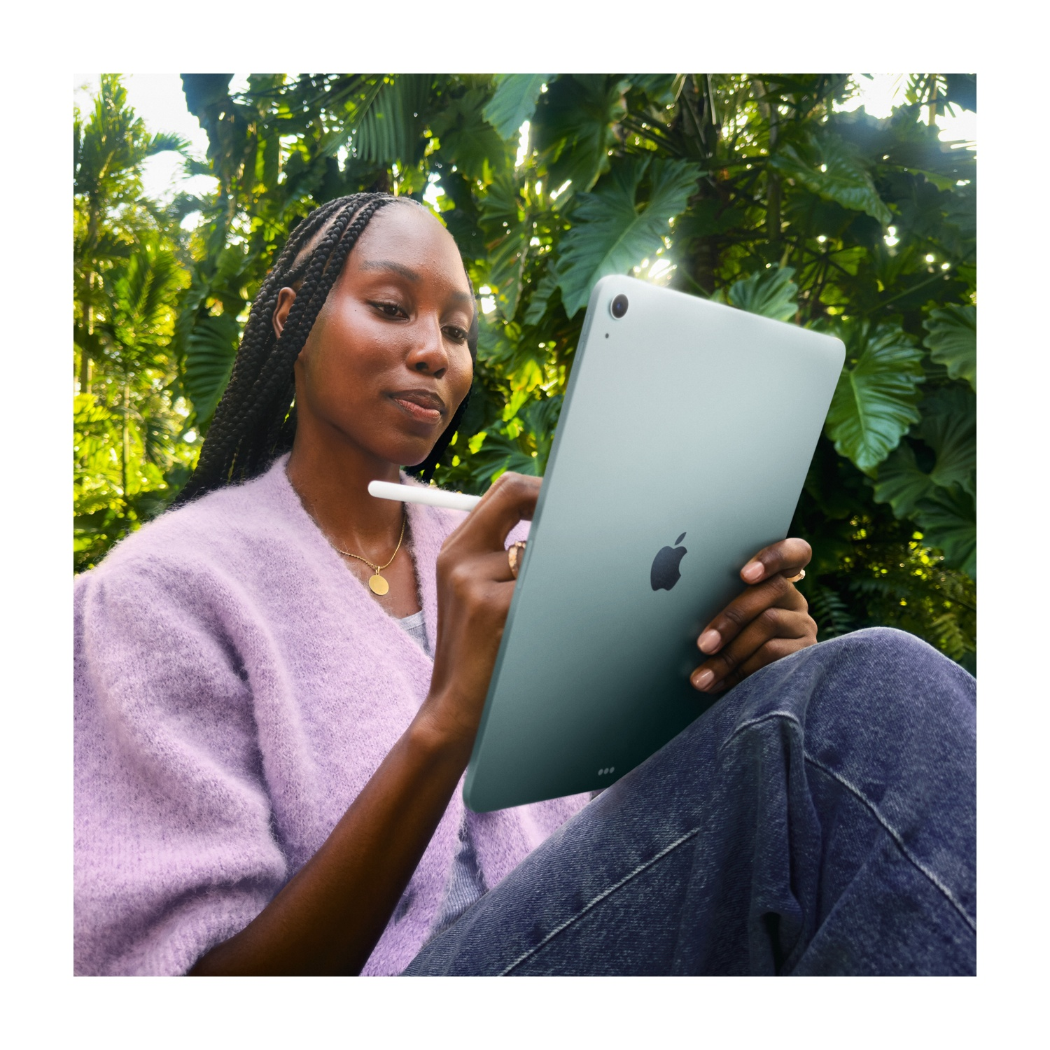 Una donna con trecce usa uno stilo su un iPad grigio. È all'aperto in un ambiente verde.