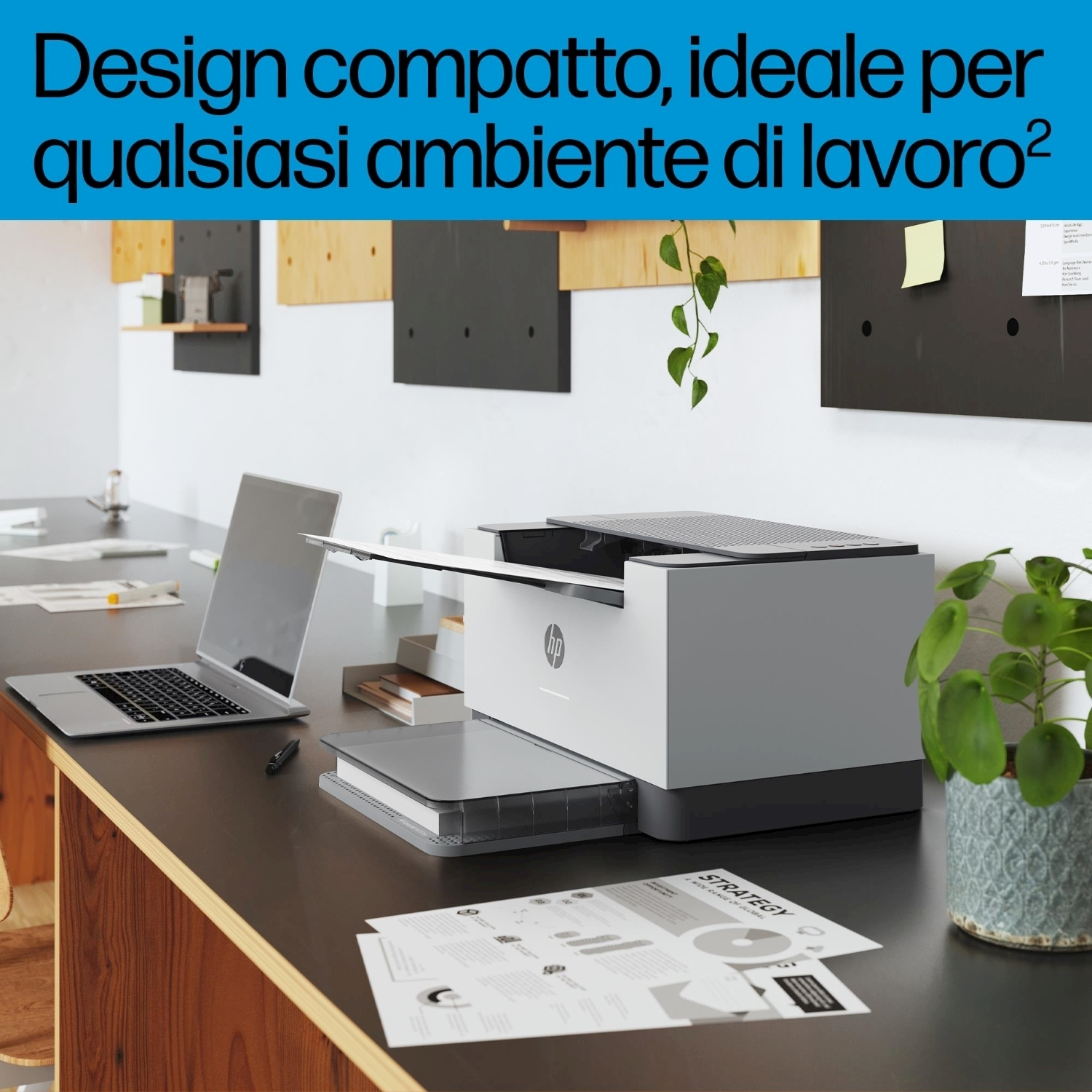 Un'area di lavoro che mostra una stampante, un laptop, carta e una pianta. La stampante è bianca, il laptop argento.