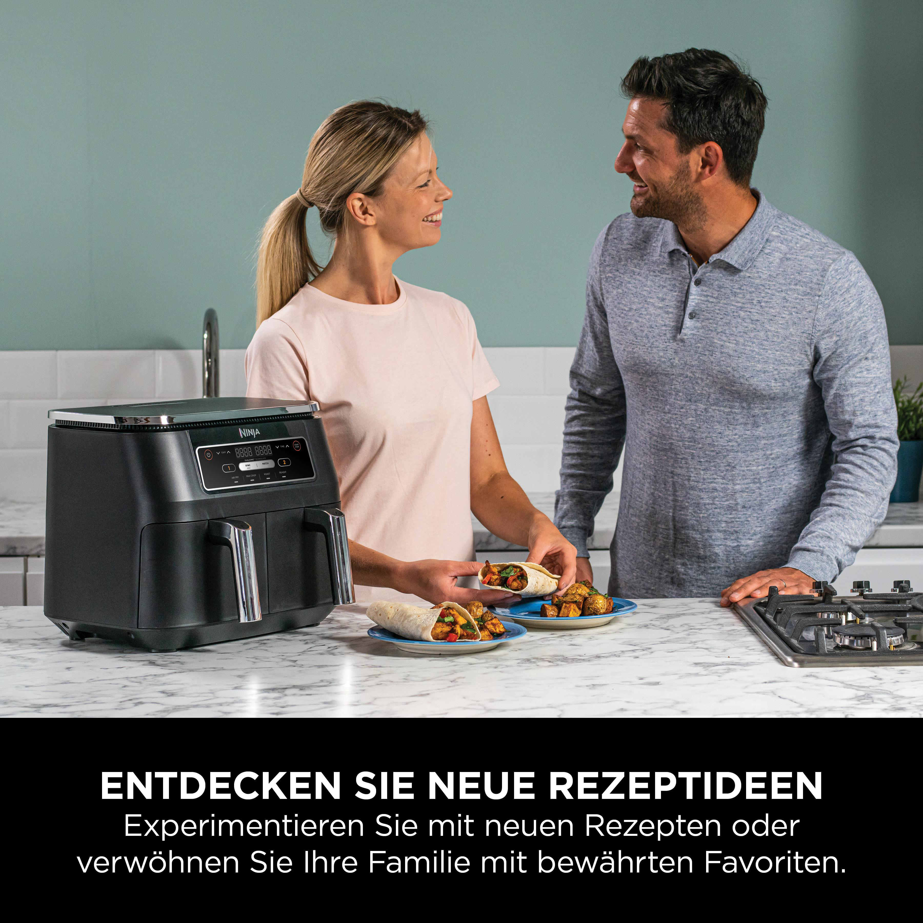 Ein Mann und eine Frau in einer Küche mit einer Heißluftfritteuse und Tellern mit Essen, die sich ansehen.