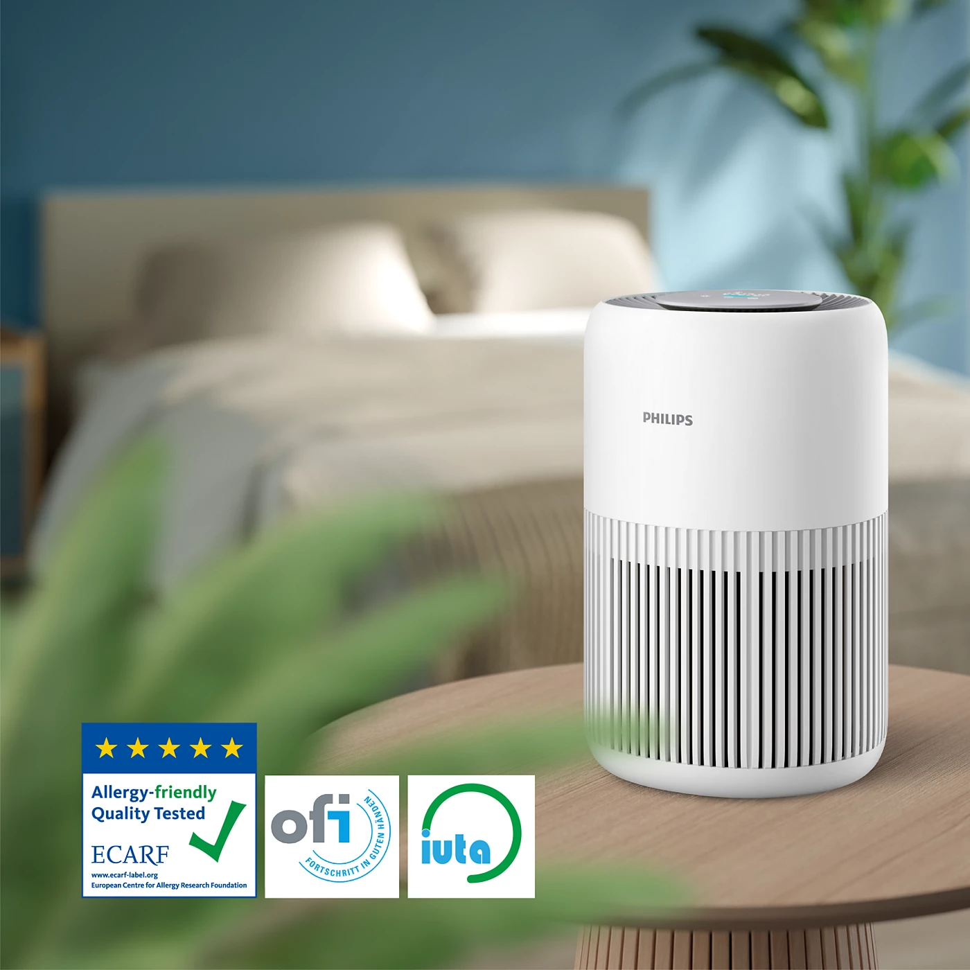 Purificateur d'air blanc sur une table en bois dans une pièce, avec logos et lit en arrière-plan.