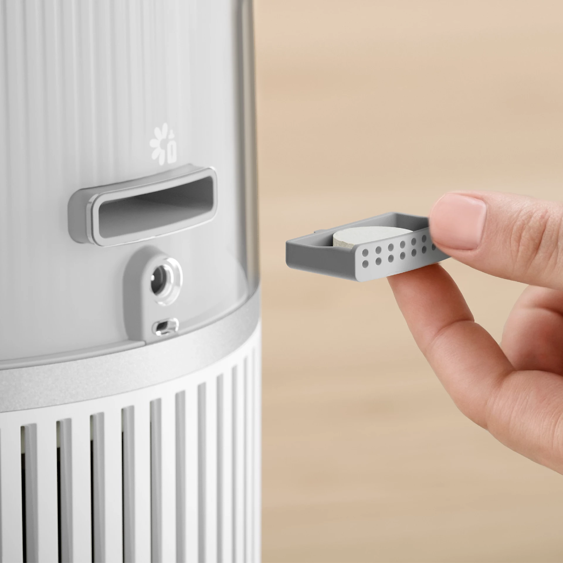 Une main tient un petit filtre gris d'un purificateur d'air. Le purificateur est gris et blanc.