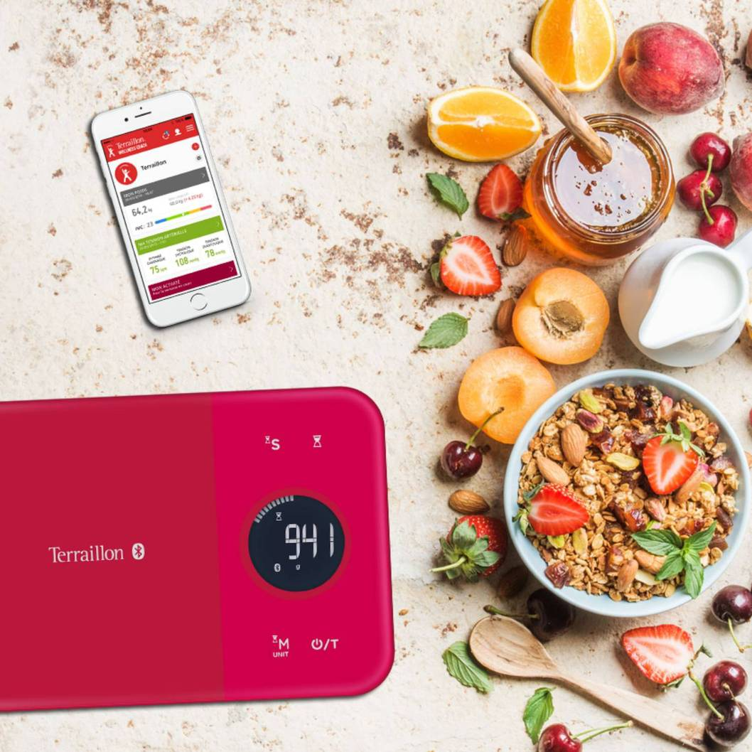 Eine rote Küchenwaage mit Essen und Smartphone, mit Früchten und Müsli.