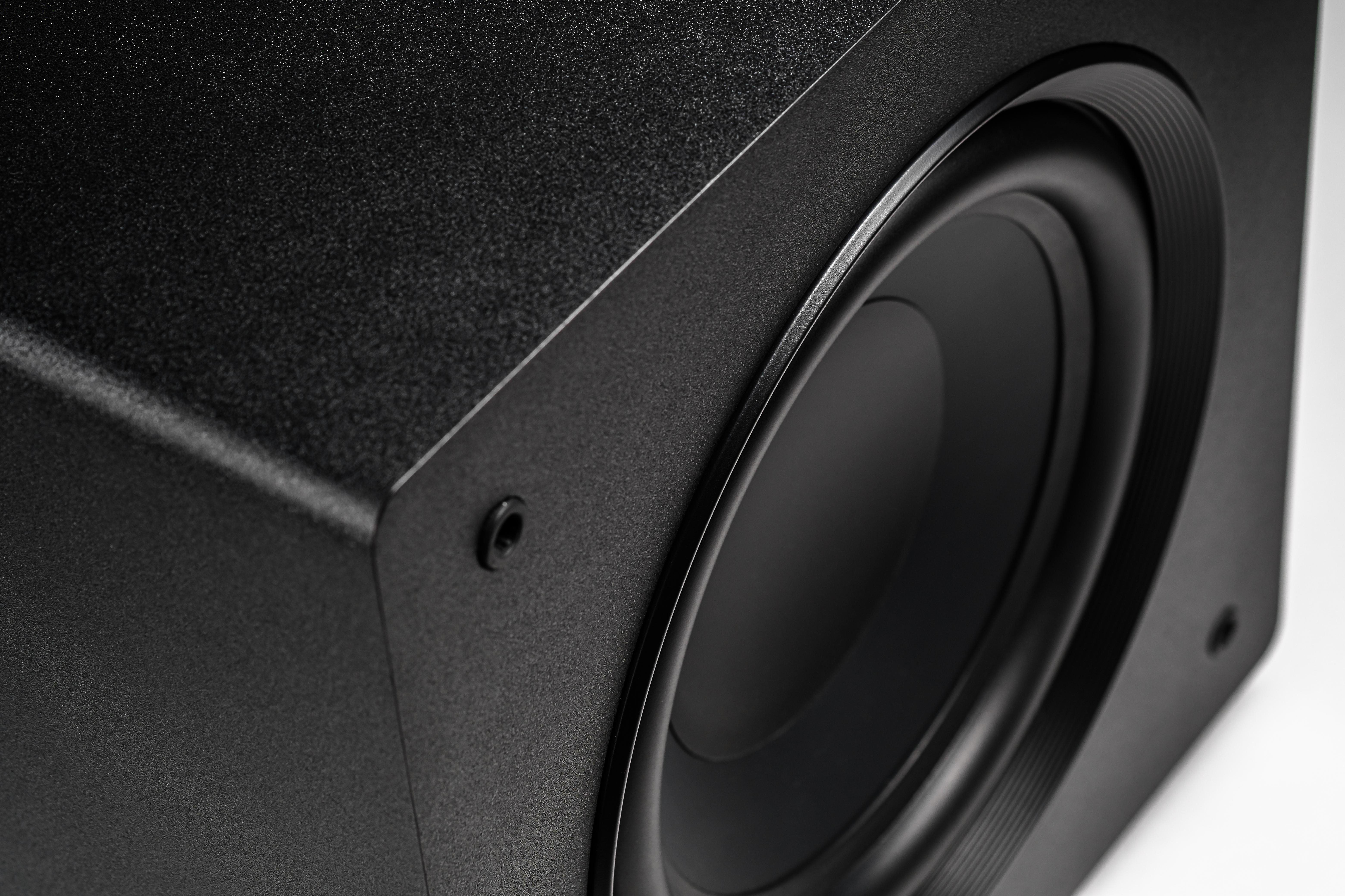 Nahaufnahme eines schwarzen Subwoofer-Lautsprechers. Der Lautsprecher hat eine strukturierte Oberfläche und eine runde Öffnung.
