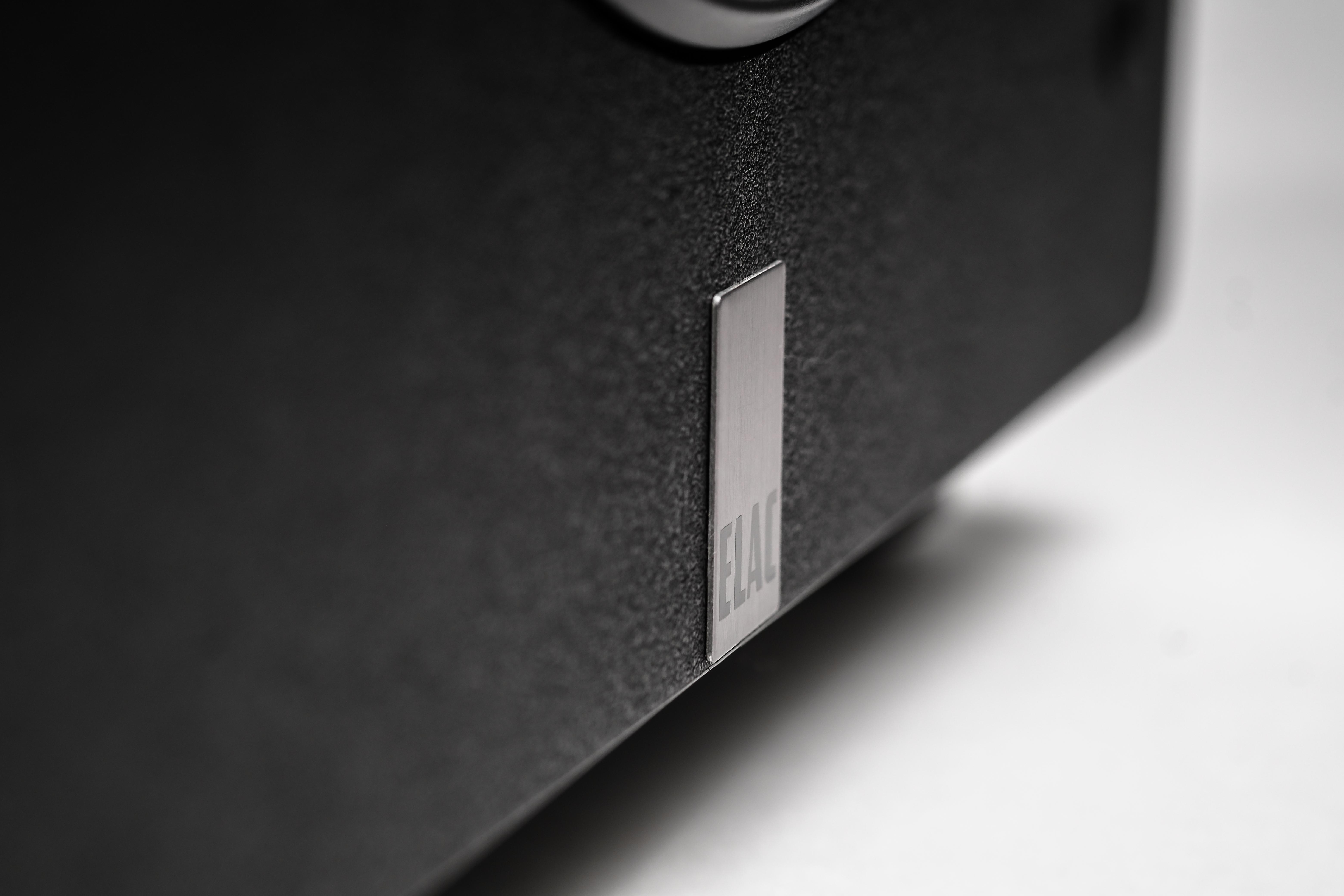Nahaufnahme eines schwarzen Lautsprechers mit ELAC-Logo. Eine silberne rechteckige Platte befindet sich an der Seite.