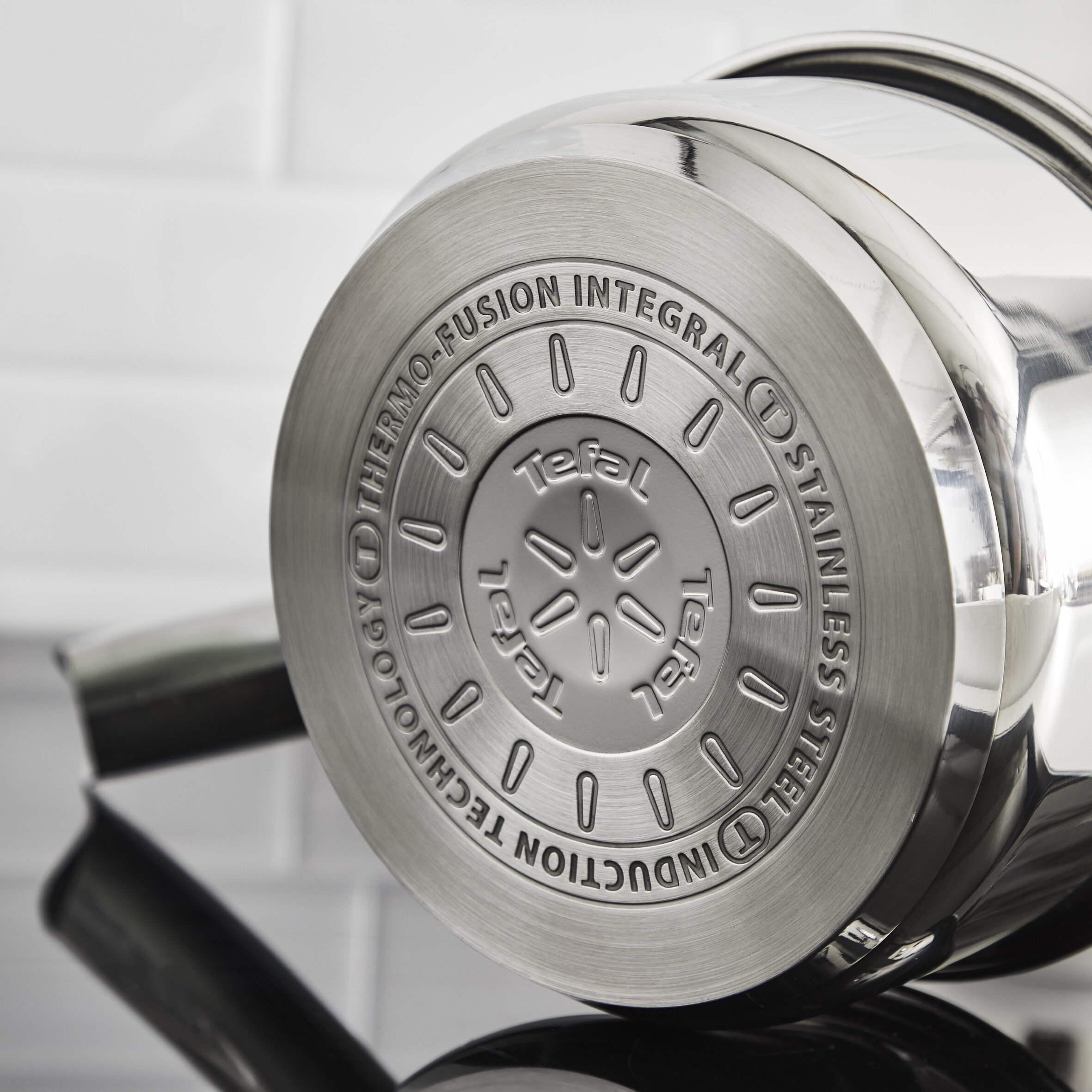 Spód garnka ze stali nierdzewnej z tekstem i okrągłym wzorem.