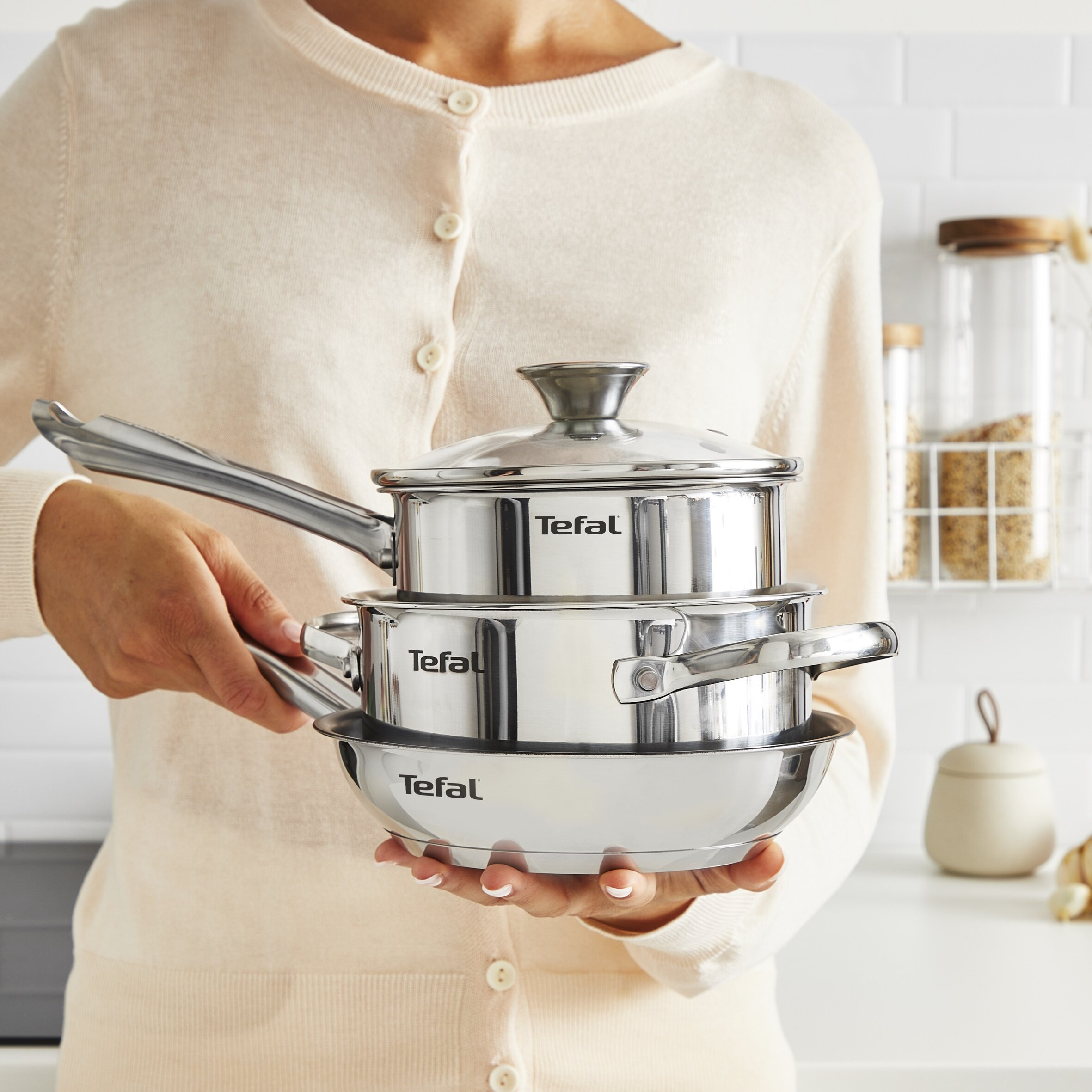 Osoba trzymająca stos trzech garnków ze stali nierdzewnej.