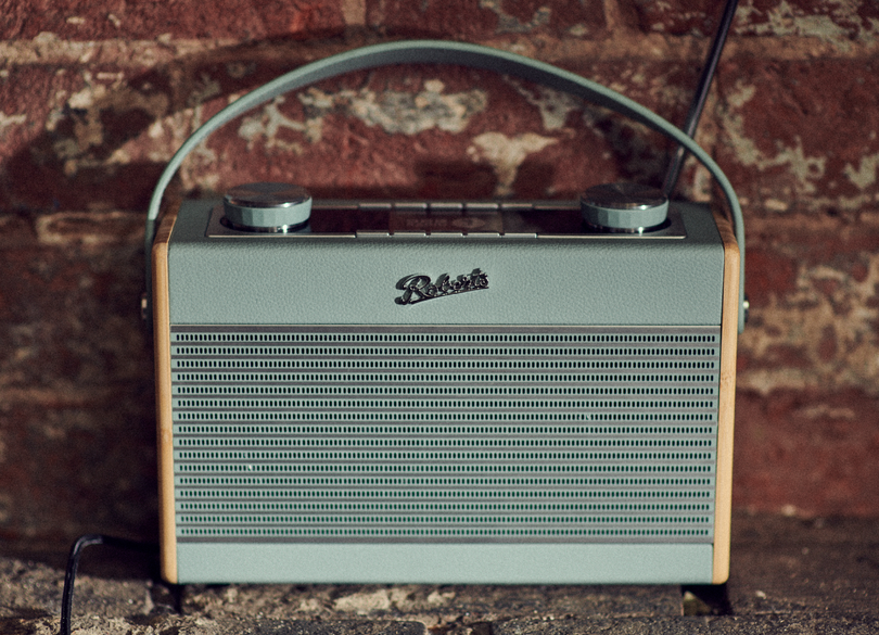Retro-Radio in Hellblau, mit Griff und Backsteinmauer im Hintergrund.