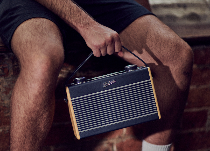 Mann hält ein Radio im Retro-Stil, mit dunkelblauer Front und Holzverkleidung.