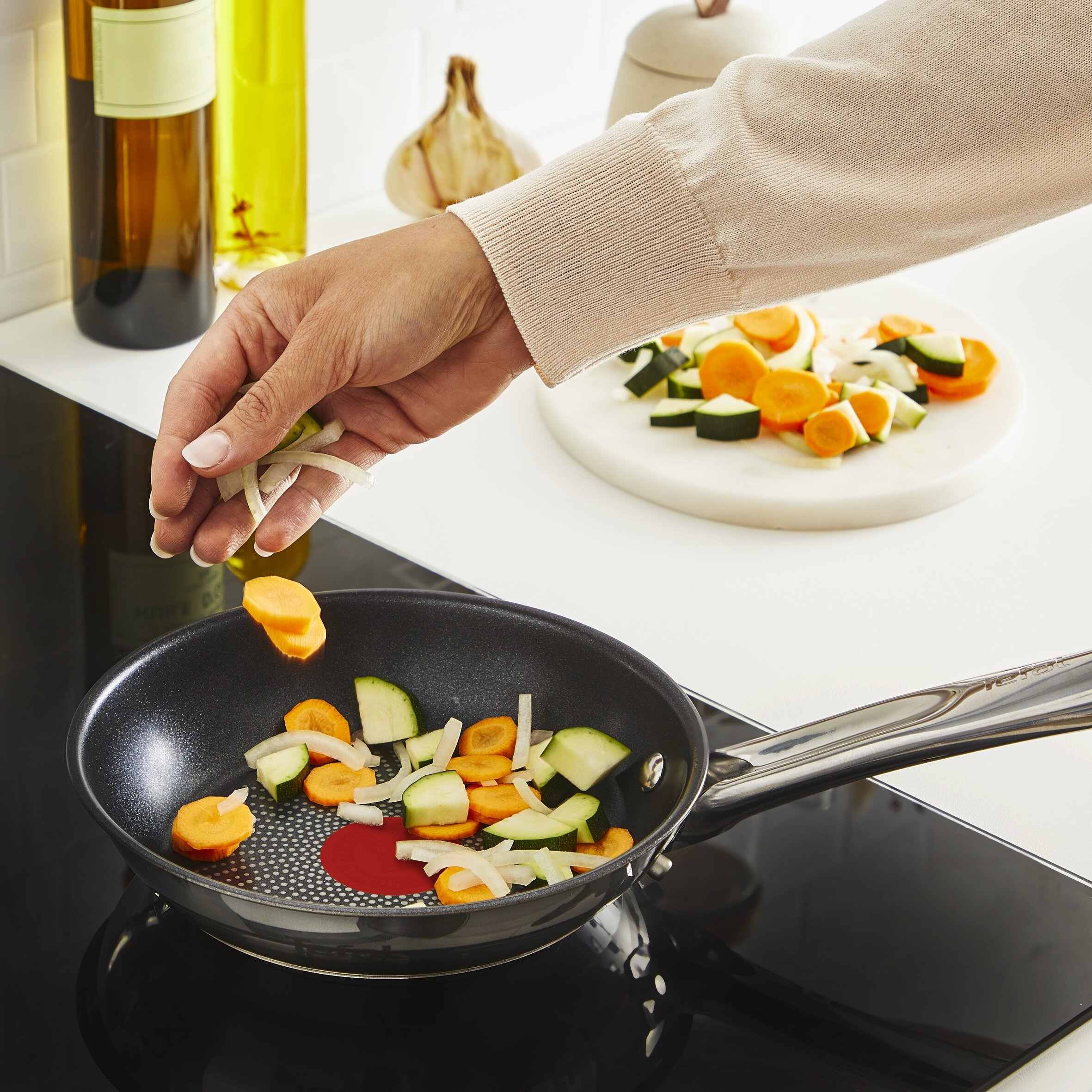 Ręka dodająca pokrojoną marchew i cukinię do patelni na kuchence.