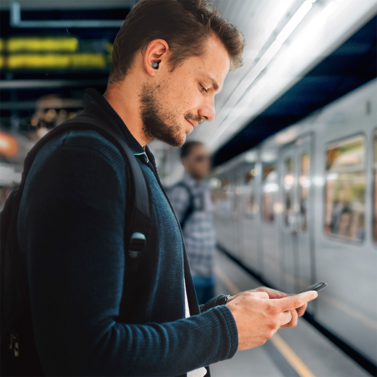 Man using a smartphone near a train station. A man is looking at his phone near a subway train.