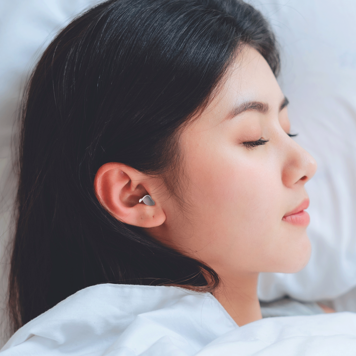 Woman sleeping with an earbud in her ear. She is lying on a pillow with her eyes closed.