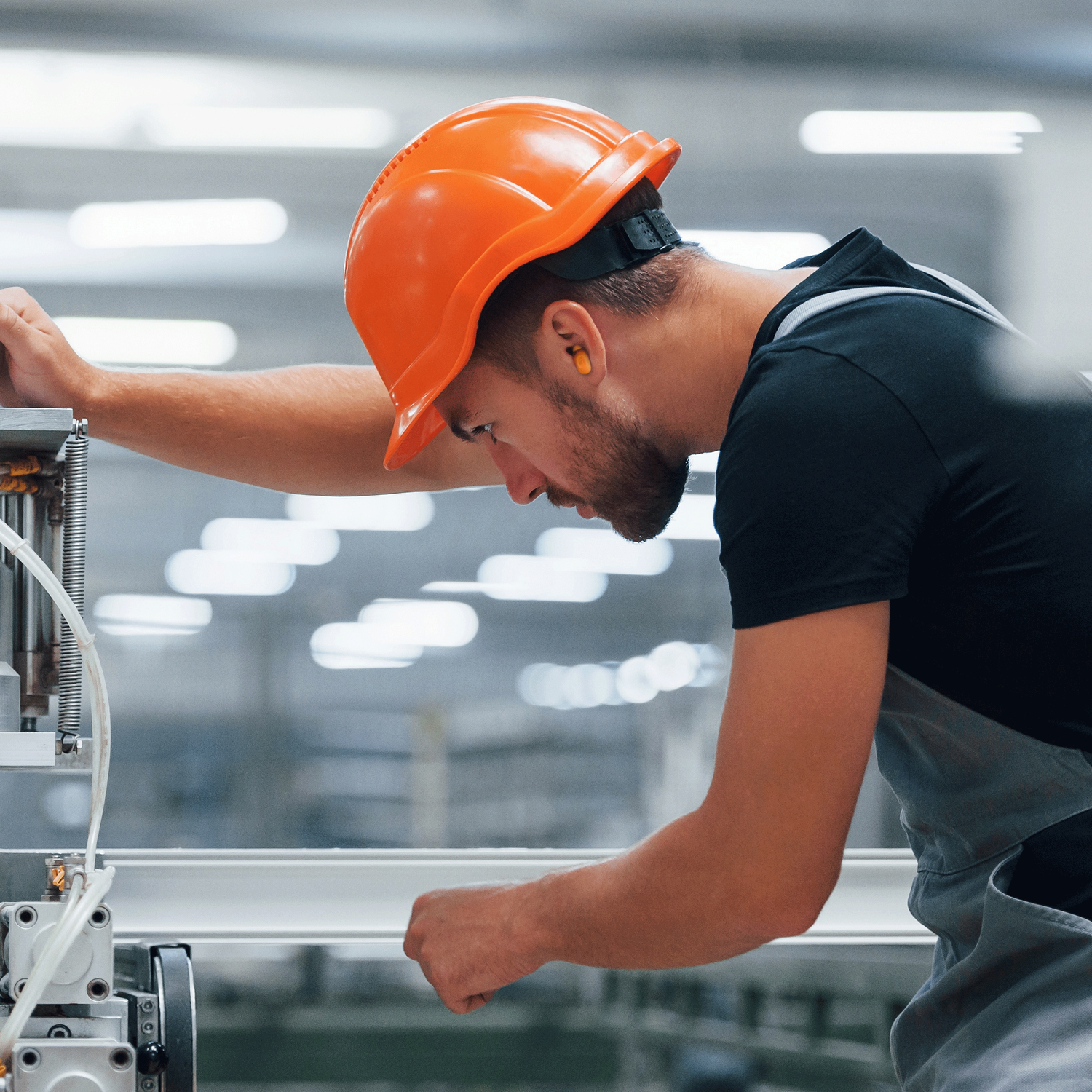 Een werknemer met een oranje helm concentreert zich op machines in een fabrieksomgeving.