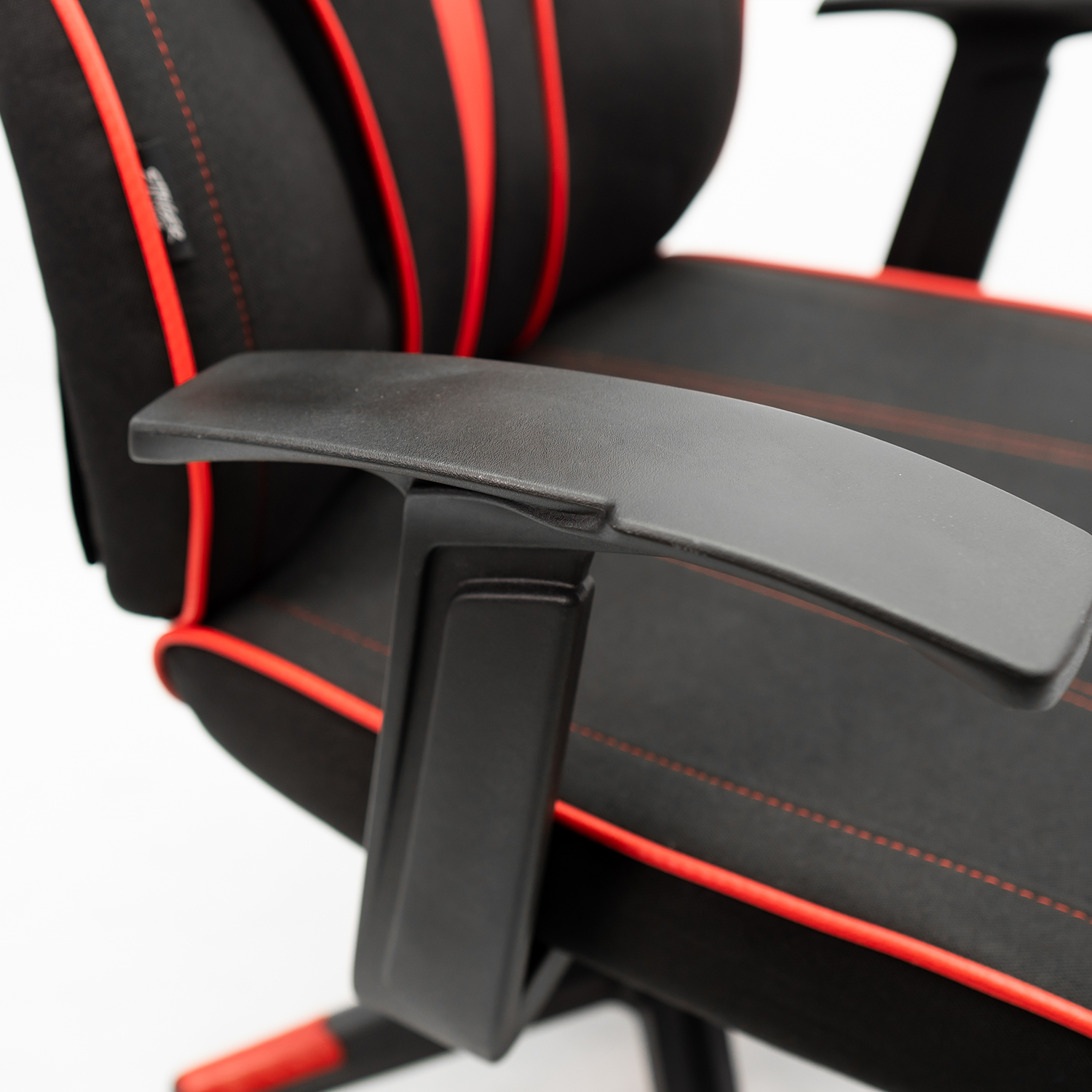 Primer plano del reposabrazos de una silla de gaming negra, con costuras rojas sobre tela negra.