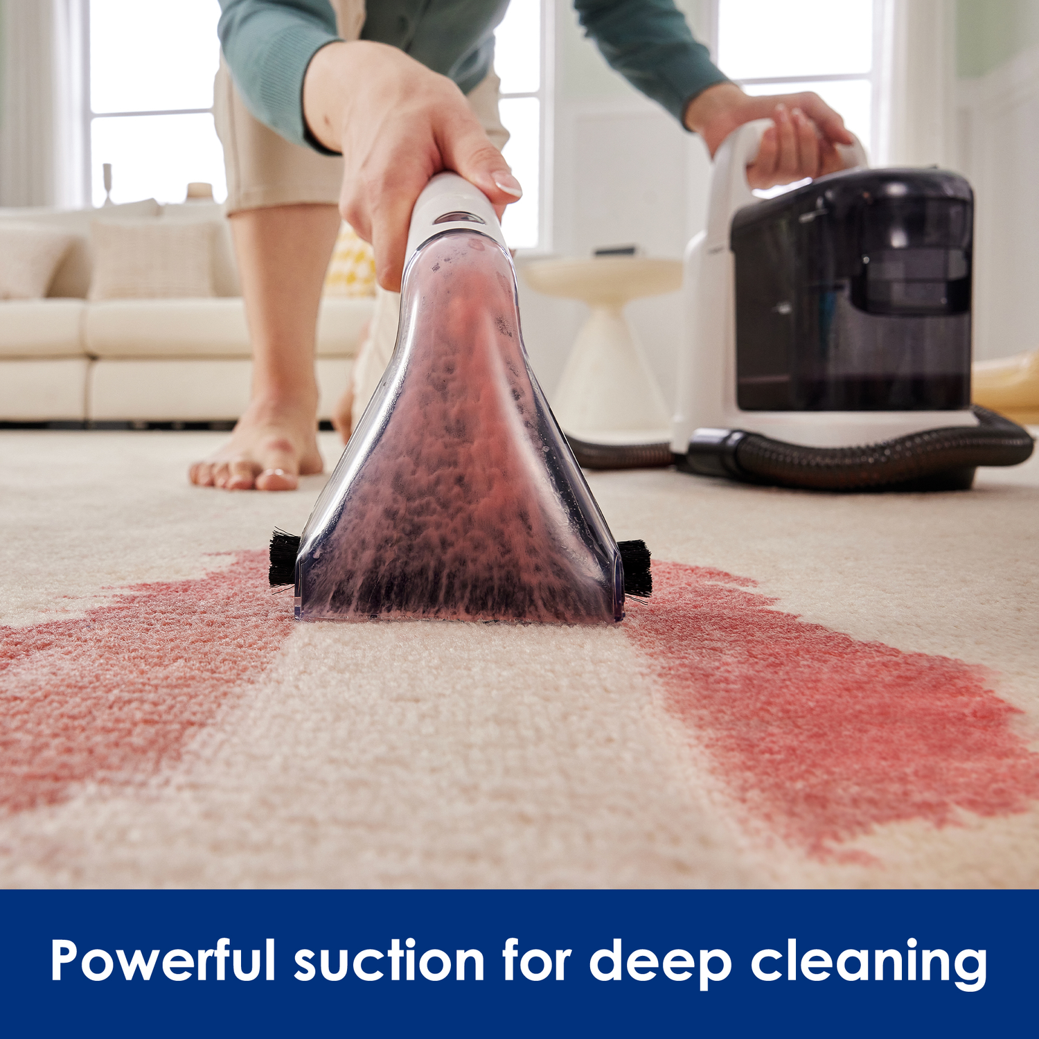 A person cleaning a red stain on carpet with a vacuum cleaner. The vacuum head is visible.