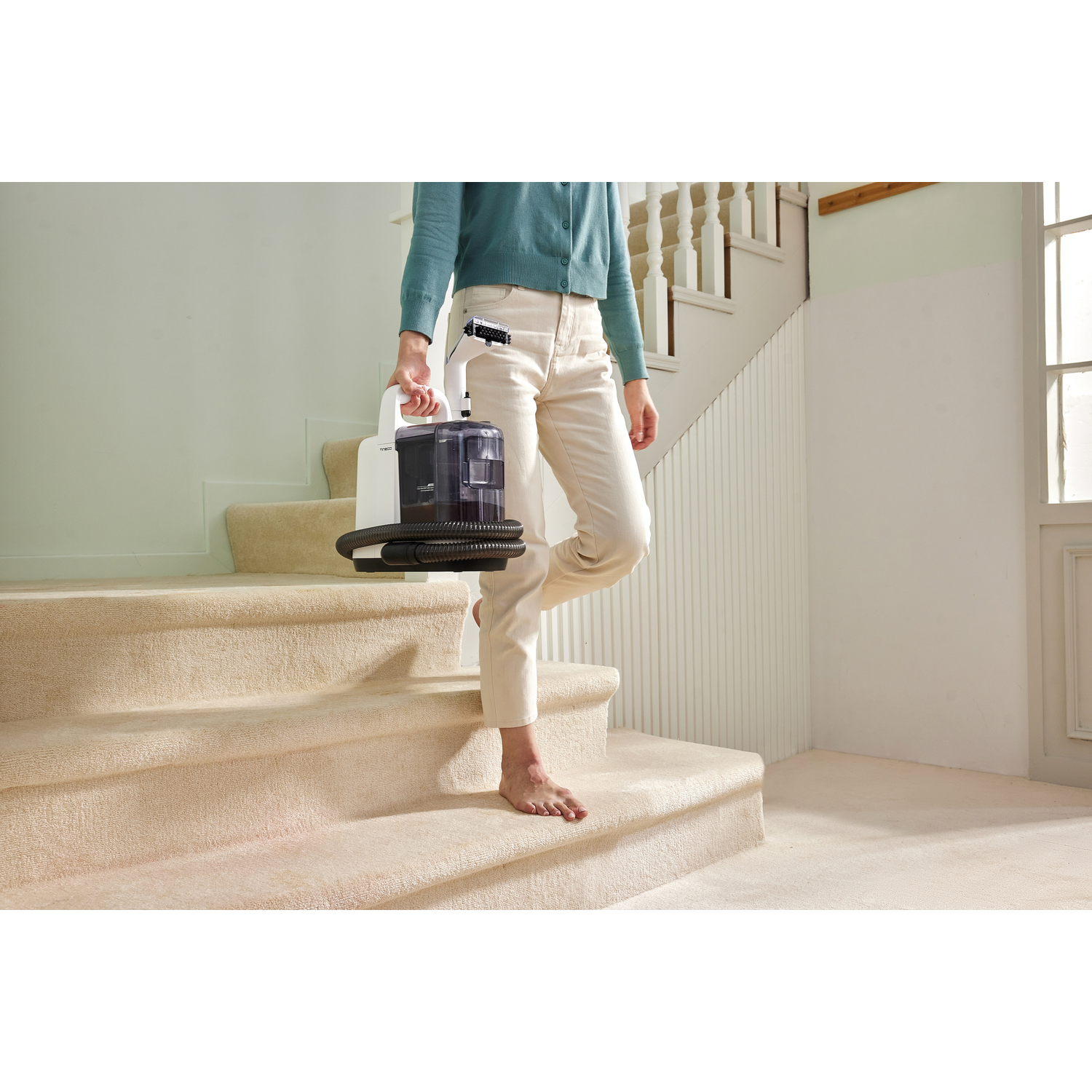 Person carrying a white portable vacuum cleaner on beige carpeted stairs.
