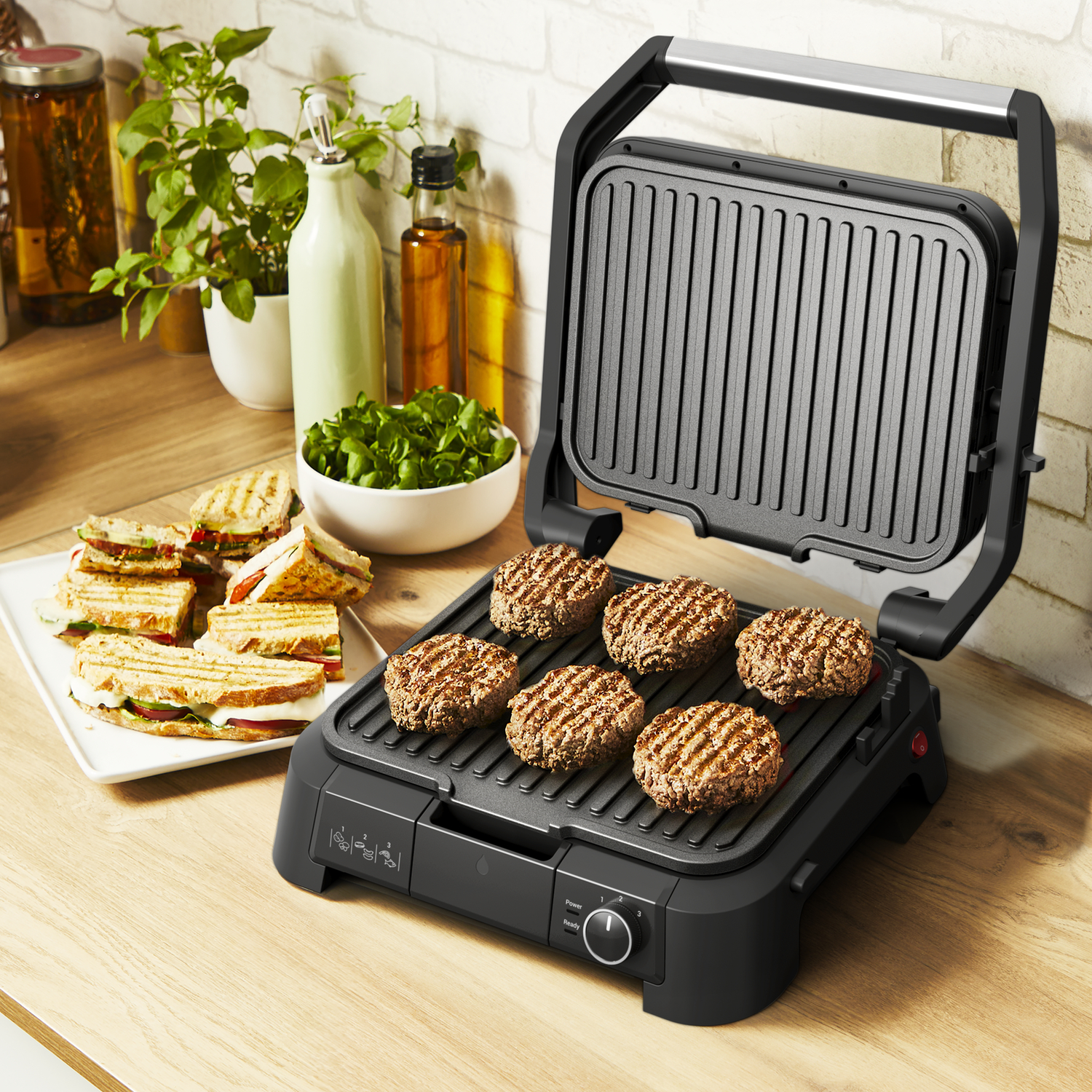 Een zwarte grill met hamburgers die bakken. Sandwiches en groenten liggen ernaast.