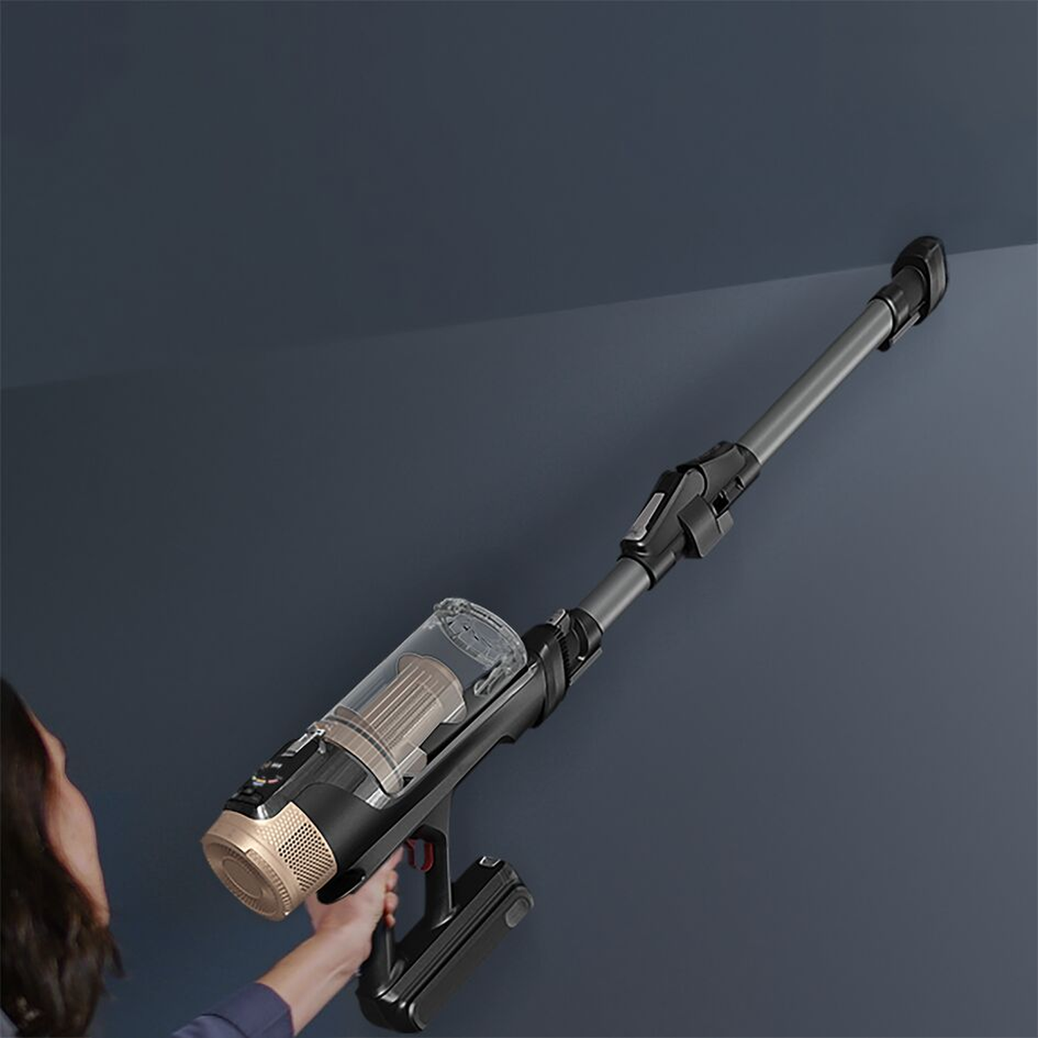 Une personne utilise un aspirateur noir et doré pour nettoyer un mur bleu foncé. L'aspirateur est incliné vers le haut.