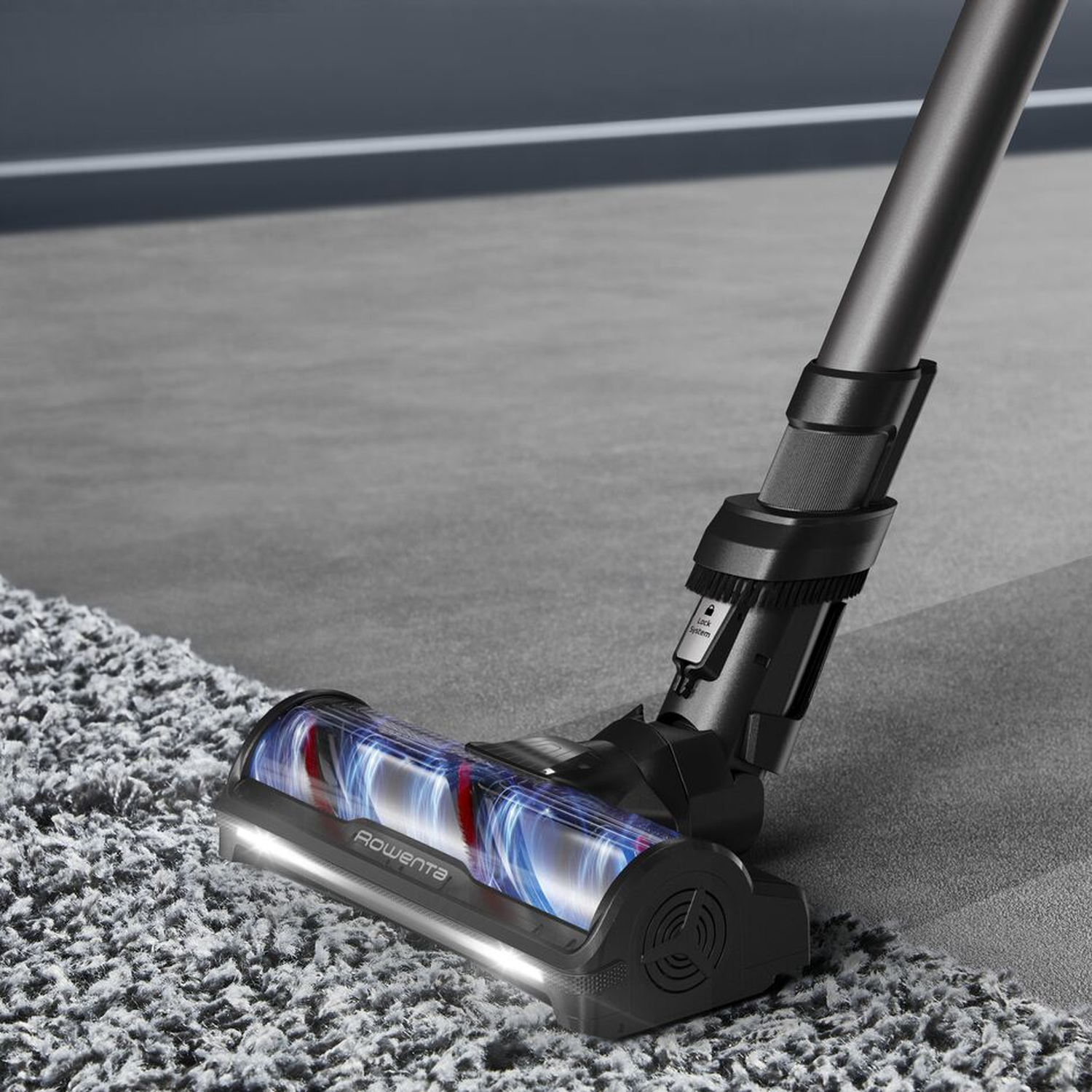 Gros plan de la tête d'un aspirateur noir sur un tapis gris. La brosse bouge.