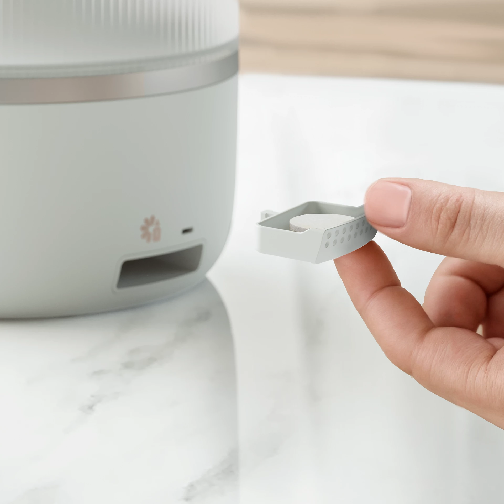 Una mano che tiene un piccolo contenitore grigio, parte di un elettrodomestico bianco.