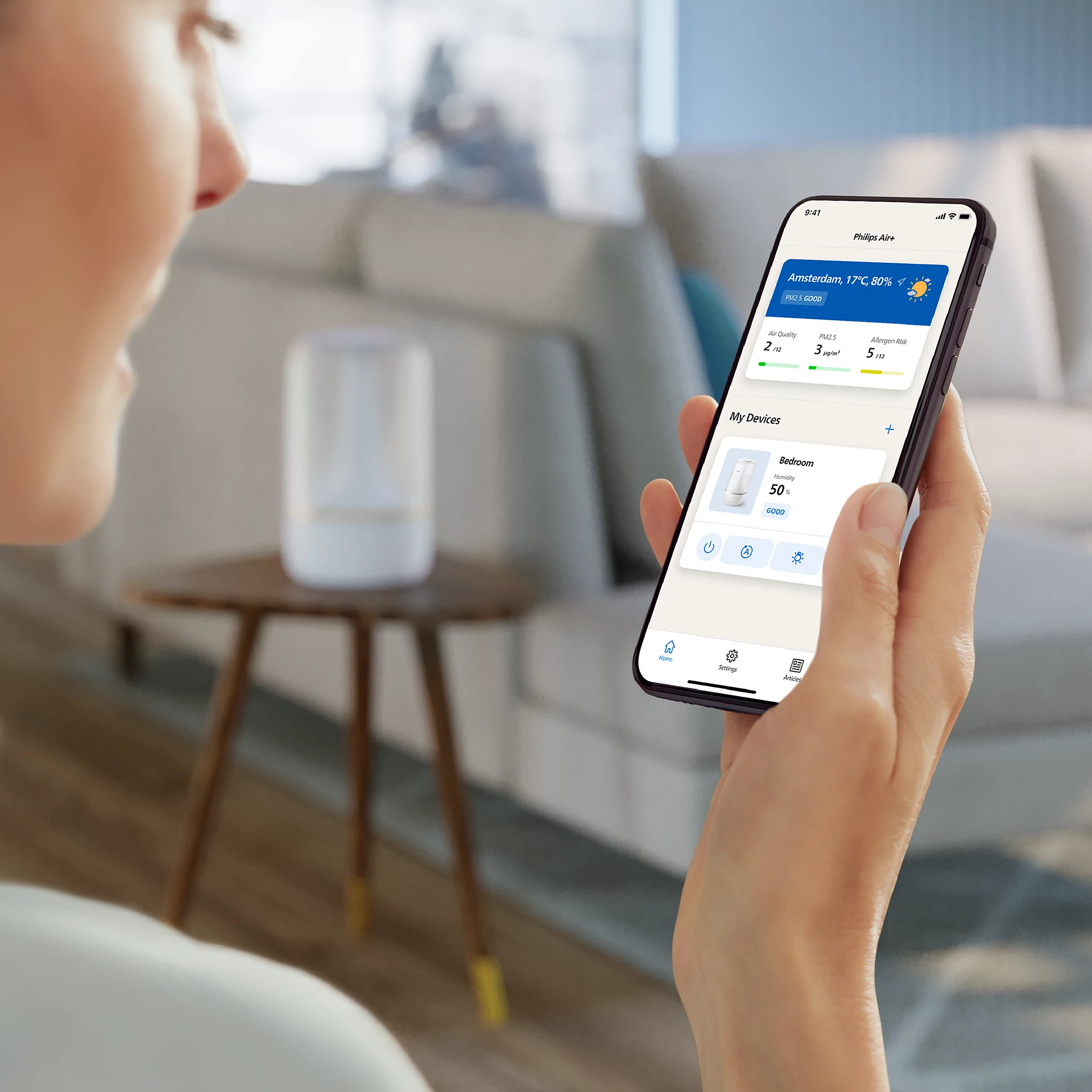 Una donna usa uno smartphone per controllare i dati sulla qualità dell'aria, con un purificatore d'aria bianco sullo sfondo.