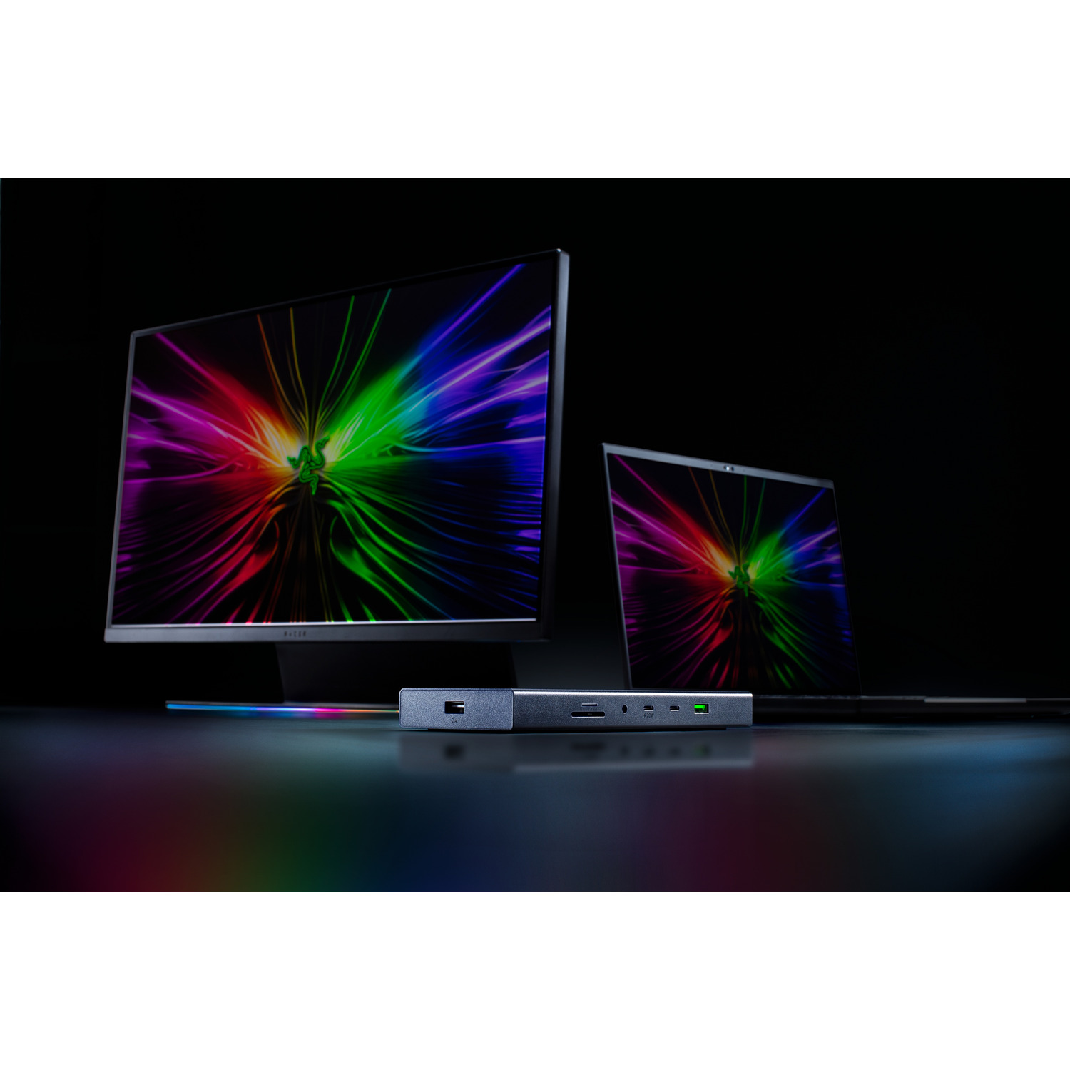 Razer monitor, laptop, and docking station on a dark surface. Displaying colorful graphics.