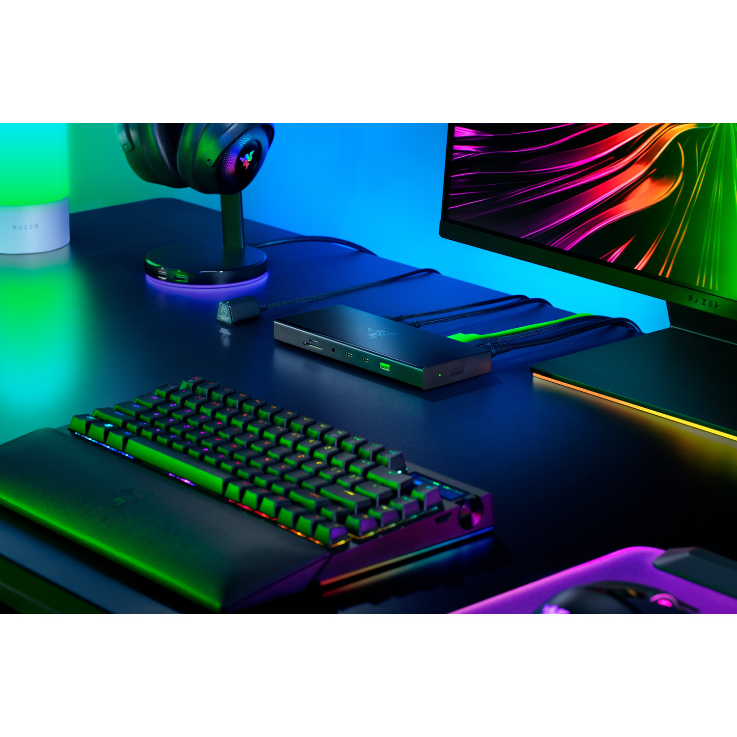 A gaming setup featuring a keyboard, mouse, headset, and a Razer dock. The background is blue.