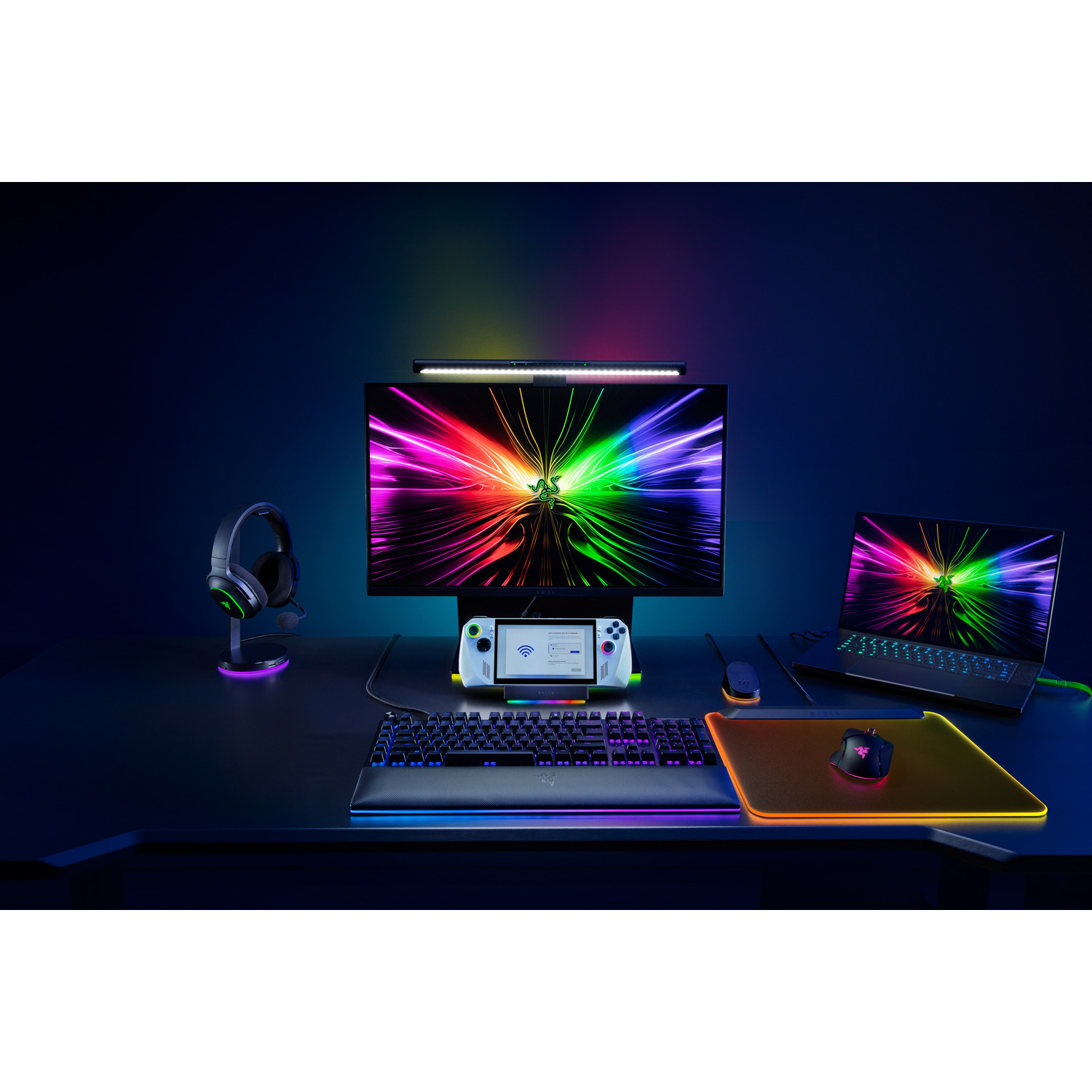 Gaming setup: monitor, headphones, keyboard, mouse, laptop, and controller, dark background.