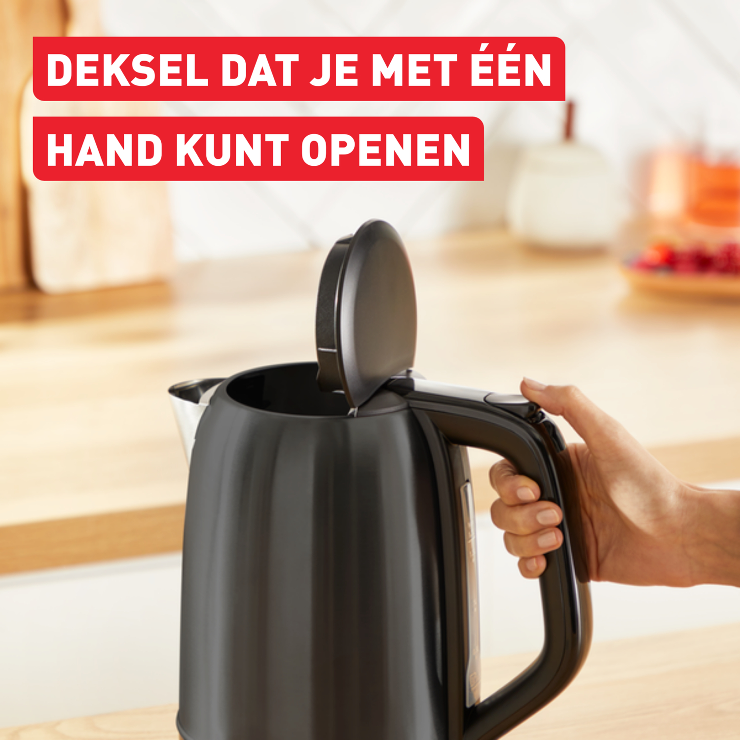 A black kettle with the lid open, a hand holding the handle, on wooden surface.
