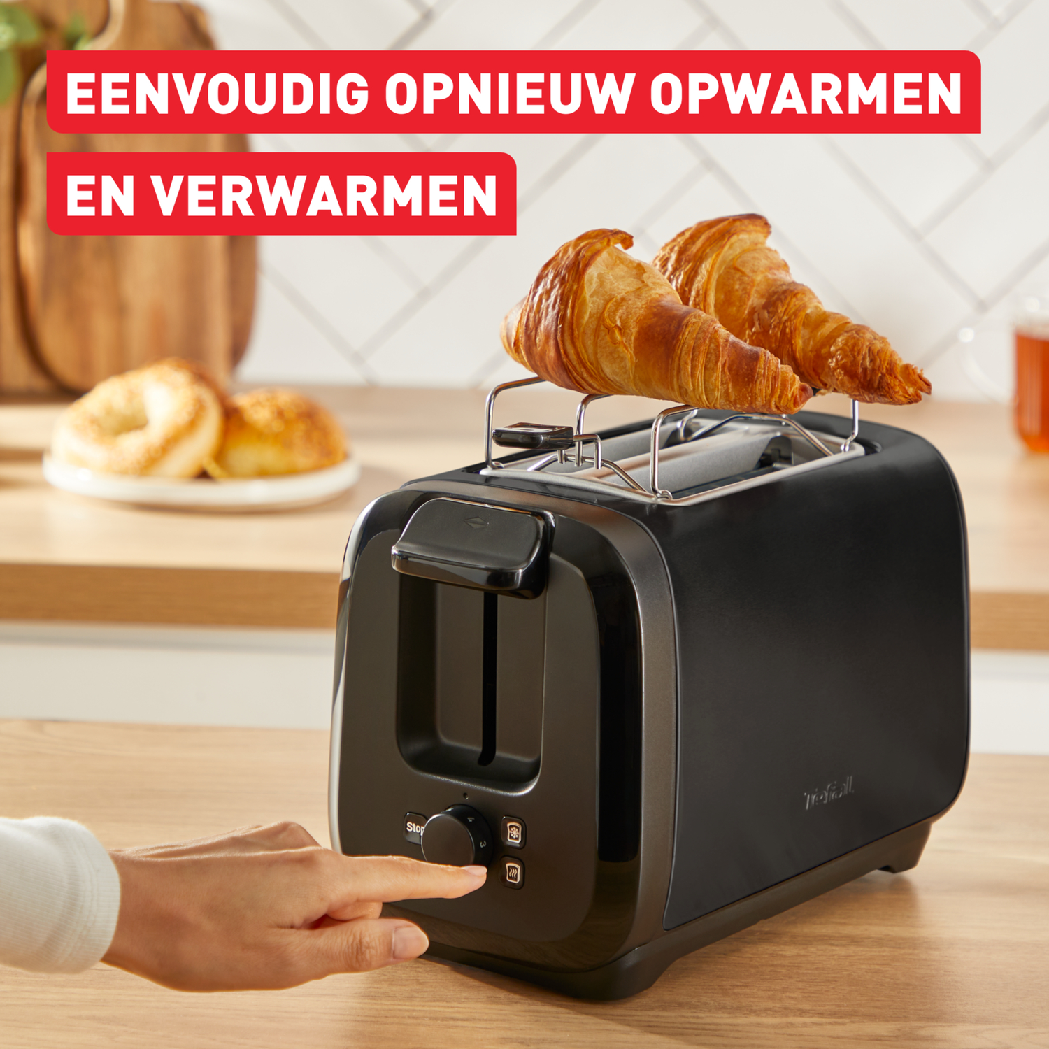Een zwarte broodrooster met croissants en een hand drukt op een knop.