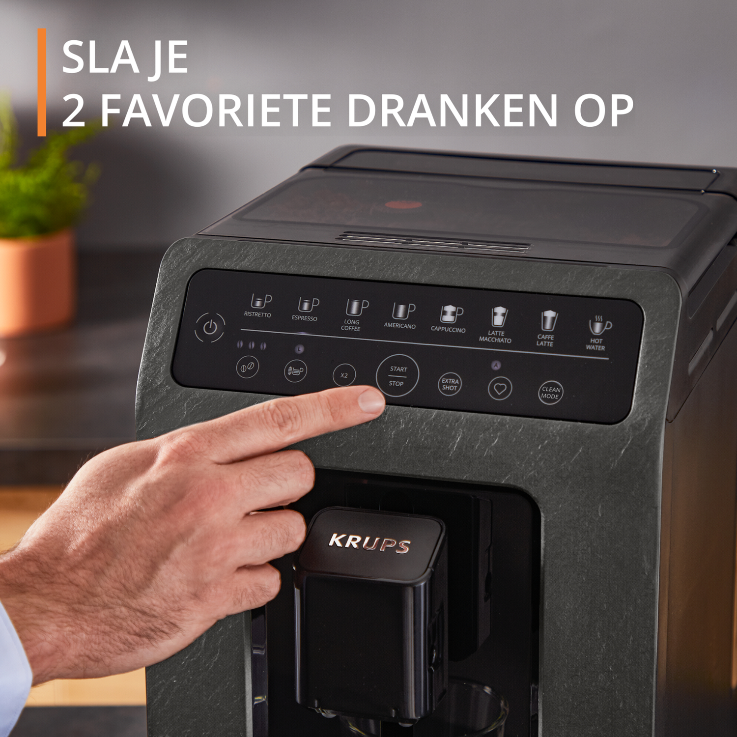 De hand van een persoon drukt op een knop op een zwart-grijze koffiemachine. Tekst: 'Krups'.