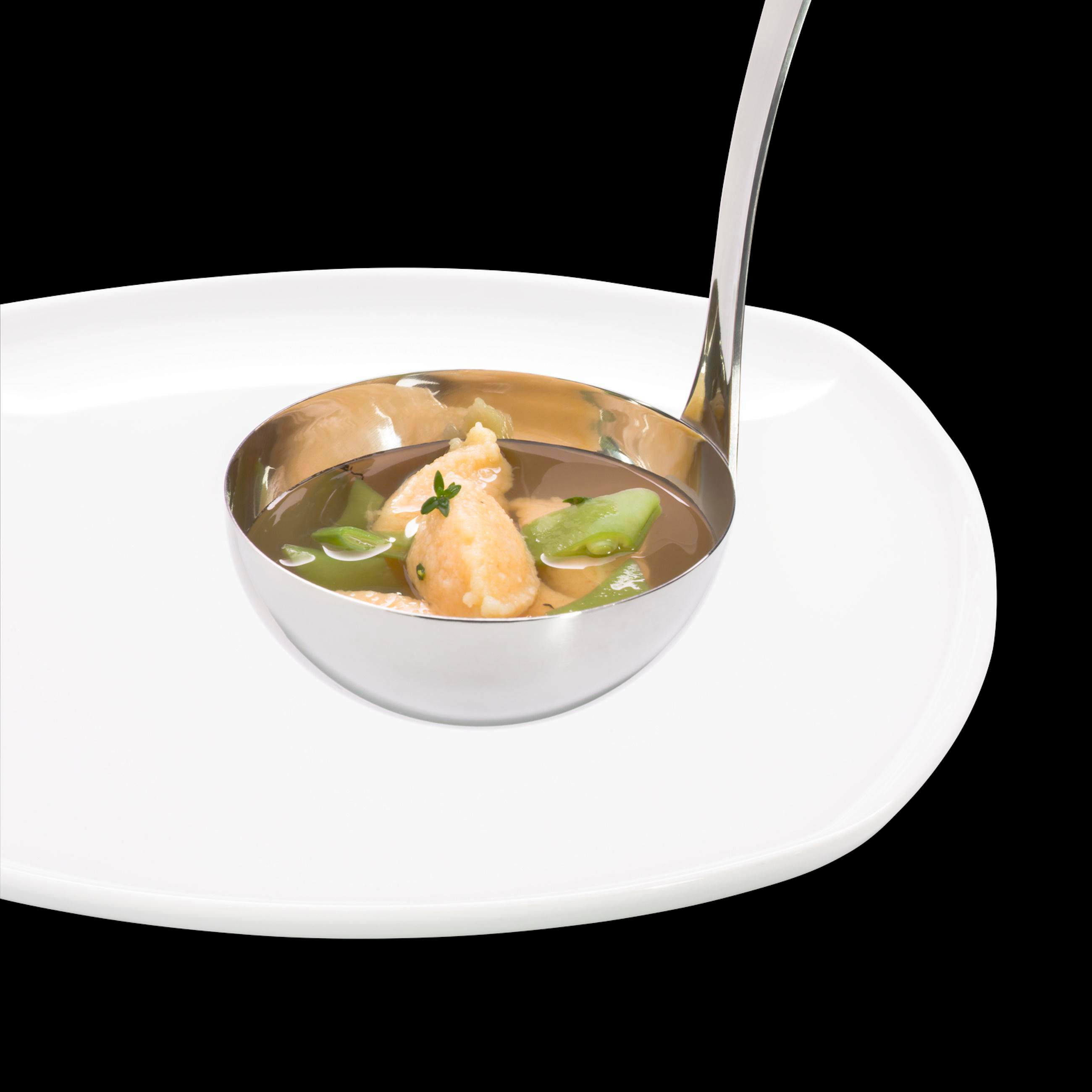 Ein silberner Löffel schöpft Suppe aus einer Schüssel auf einem weißen Teller, schwarzer Hintergrund.