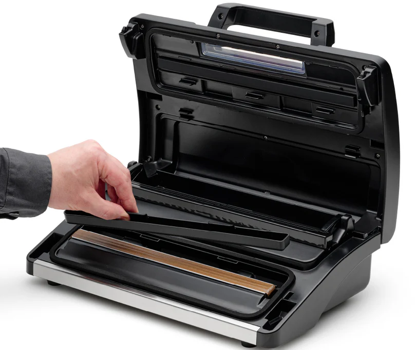 Die Hand einer Person legt ein Tablett in ein schwarzes Vakuumiergerät.