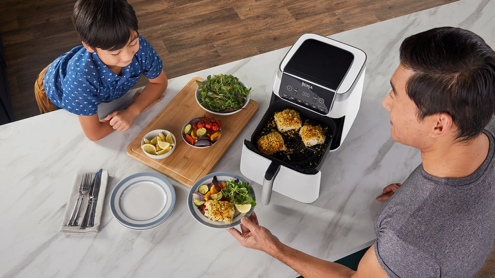 Egy férfi és egy fiú ételt készítenek egy fekete-fehér Ninja légkeveréses sütővel.