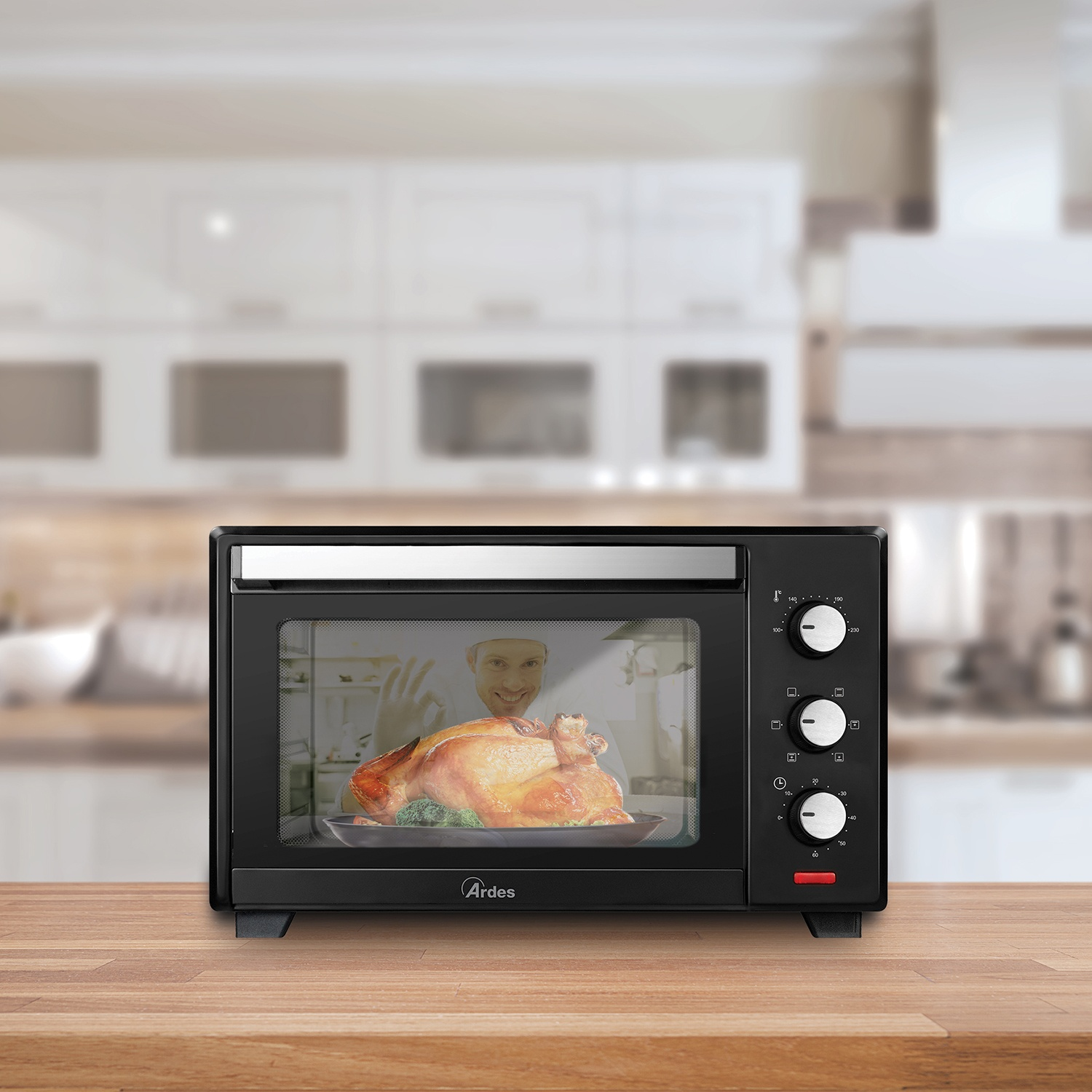 Un forno nero con un pollo arrosto dentro. Un uomo sorride dall'interno del forno su un tavolo di legno.